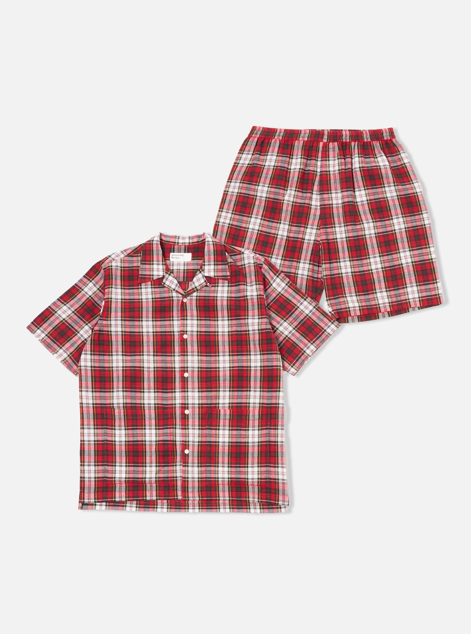 The Red Madras Check Short Pyjama Set. The set is red, white, and black plaid. The shirt is button-down and short-sleeved. The shorts have an elastic waistband. Set on a white background.