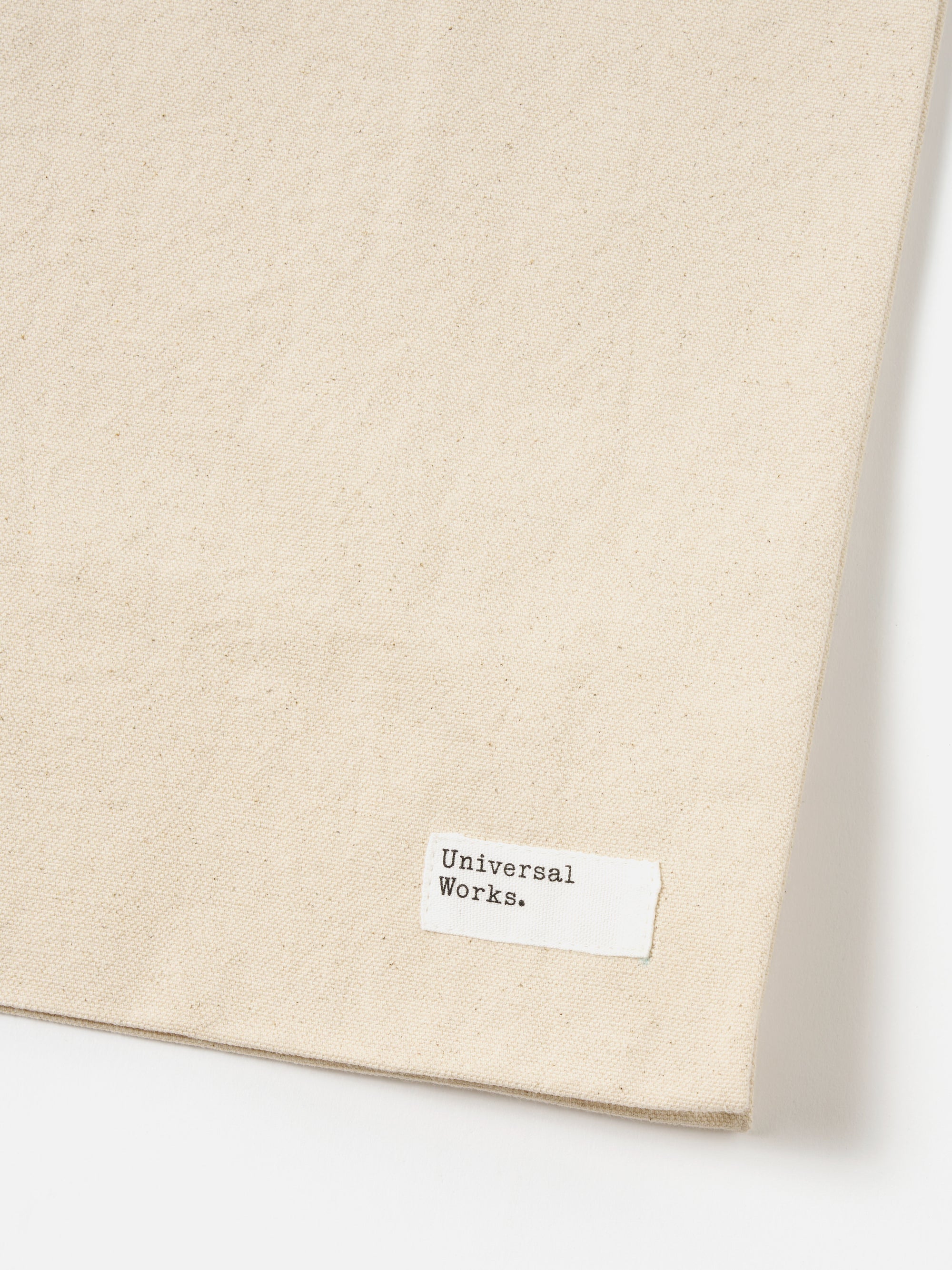 Close-up of an Ecru Canvas Market Tote on a white background. The canvas is a light beige color. A small white tag with "Universal Works." is sewn on.