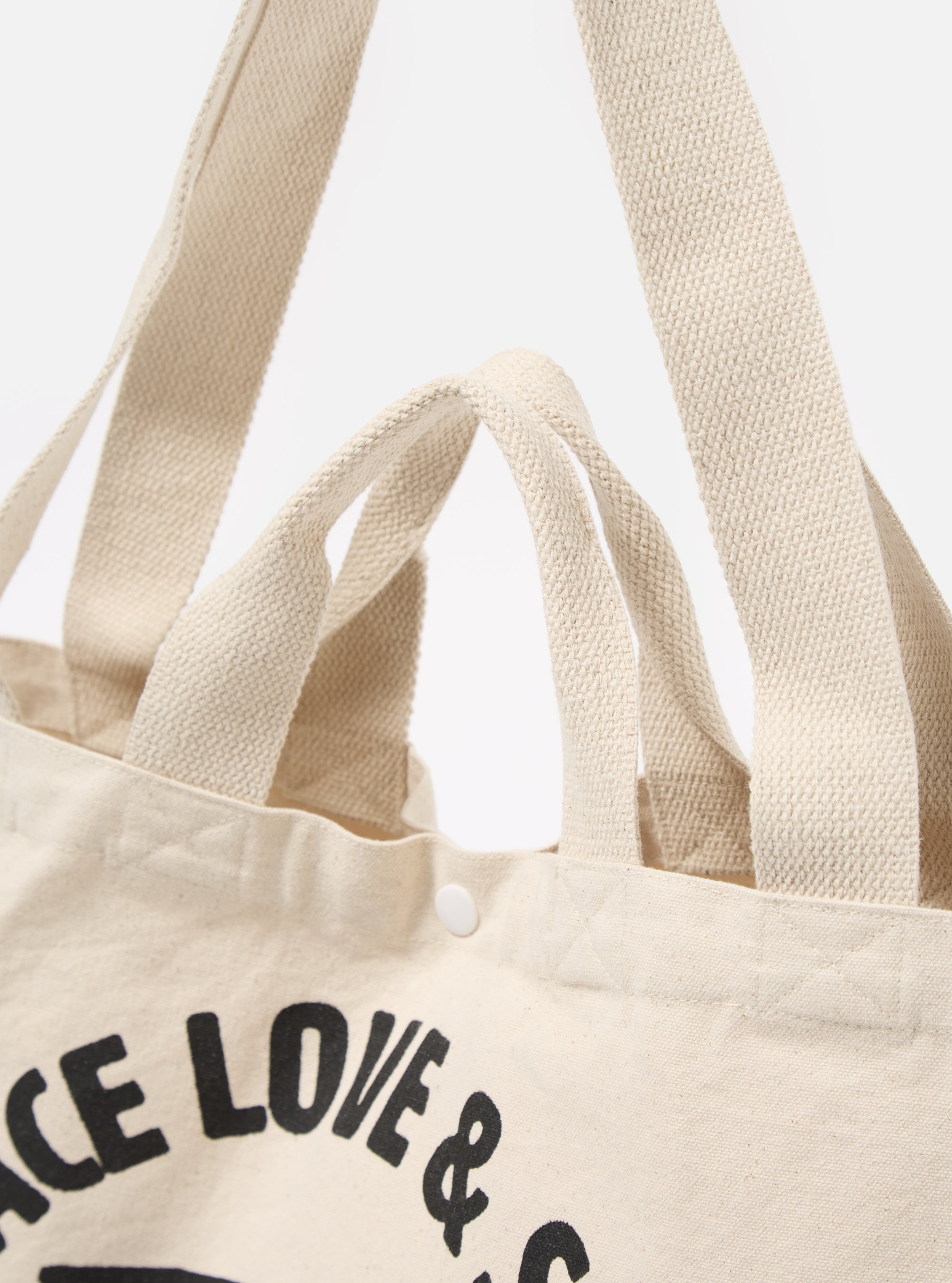 Close-up of an Ecru Canvas Market Tote against a white background. The tote is made of ecru canvas with matching handles. The bag features a snap closure.