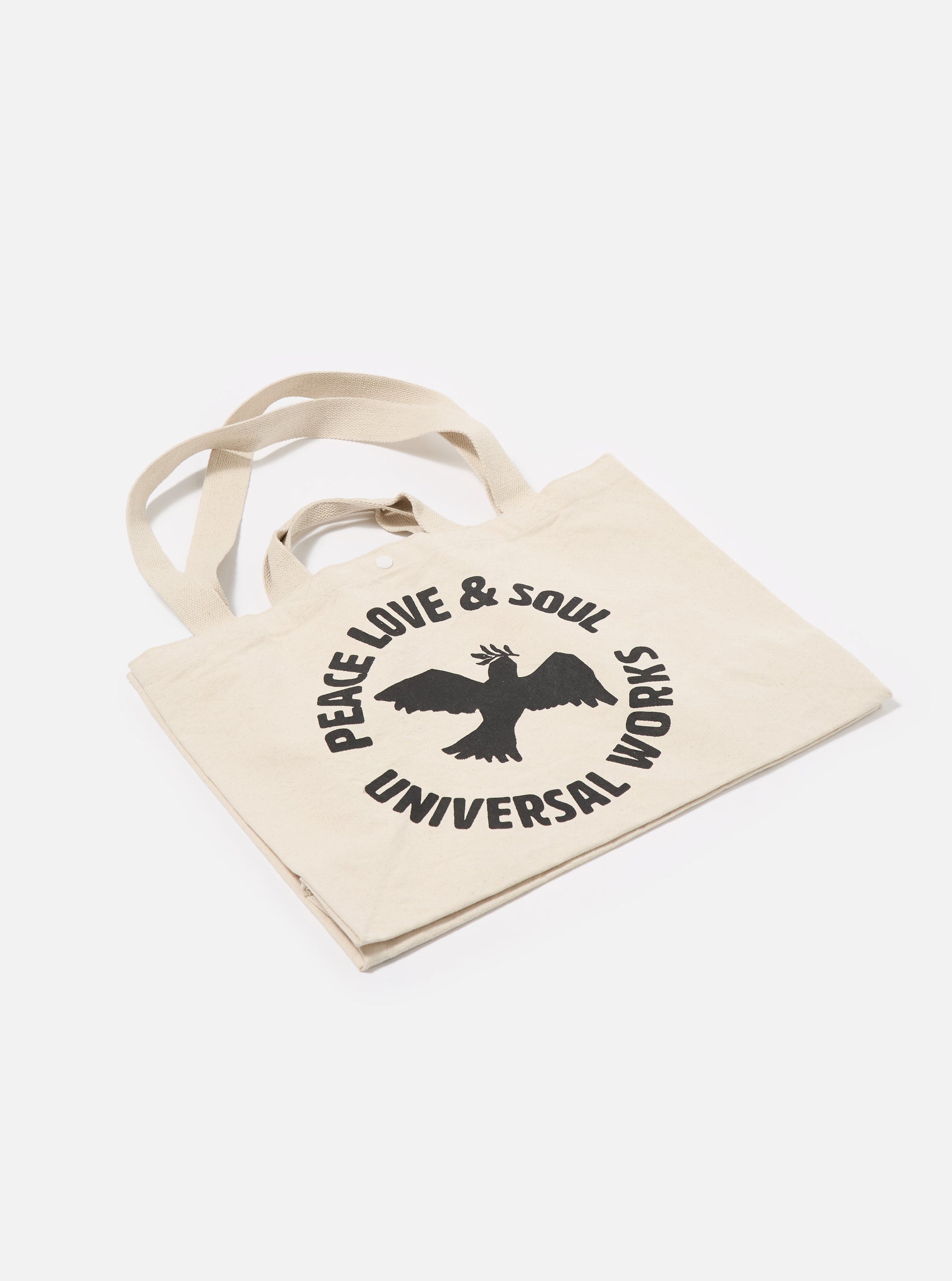 The Ecru Canvas Market Tote bag on a white surface. The bag is ecru-colored canvas with black text and a bird graphic. The background is a clean, minimalist white.