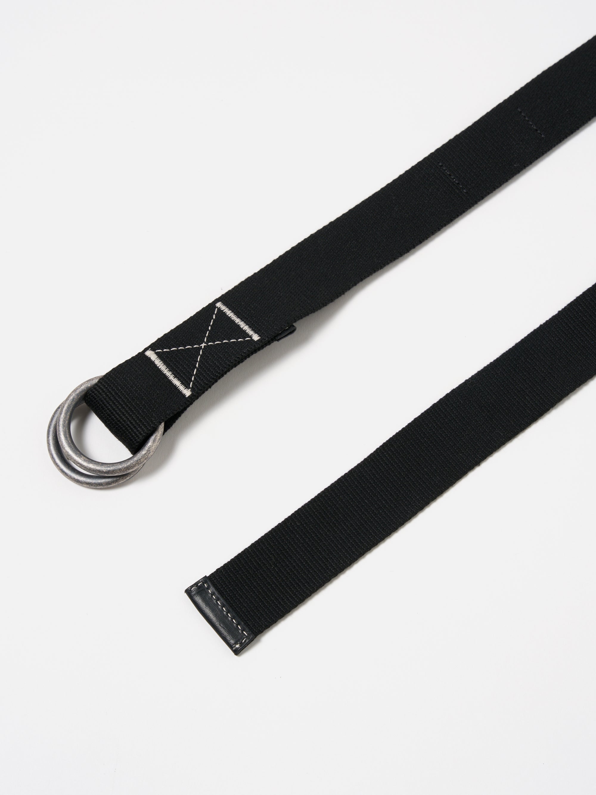 Close-up of a Black Canvas O Ring Belt on a white surface. The belt is made of black canvas with silver O-rings. The end of the belt has a black leather finish.
