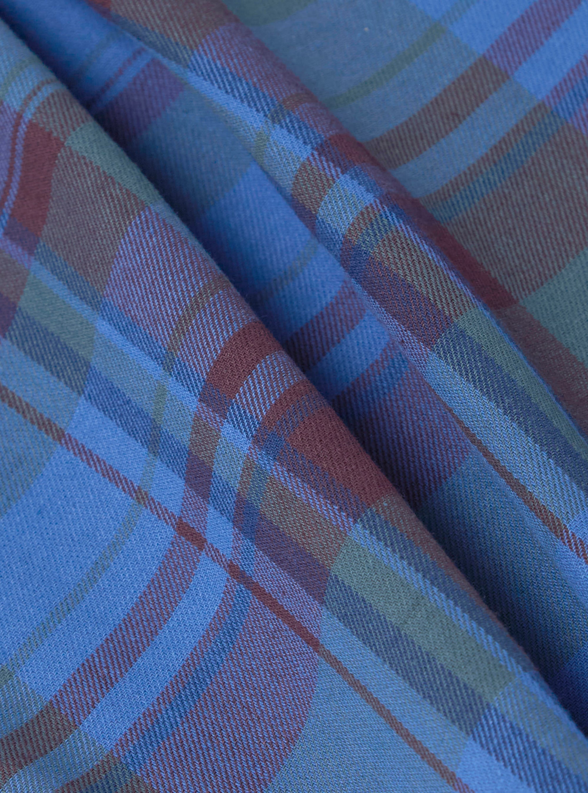 Close-up of the Multi Kip Check 3 Pack Boxer Short fabric. The blue, brown, and green plaid material is folded on a plain surface, showing the texture and pattern.