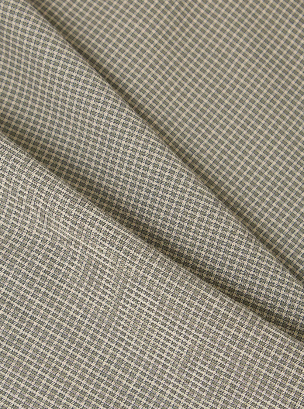 Close-up of the Green Tiny Check Boxer Short fabric. The material is a light beige with a small green check pattern. The fabric is folded on a plain surface.