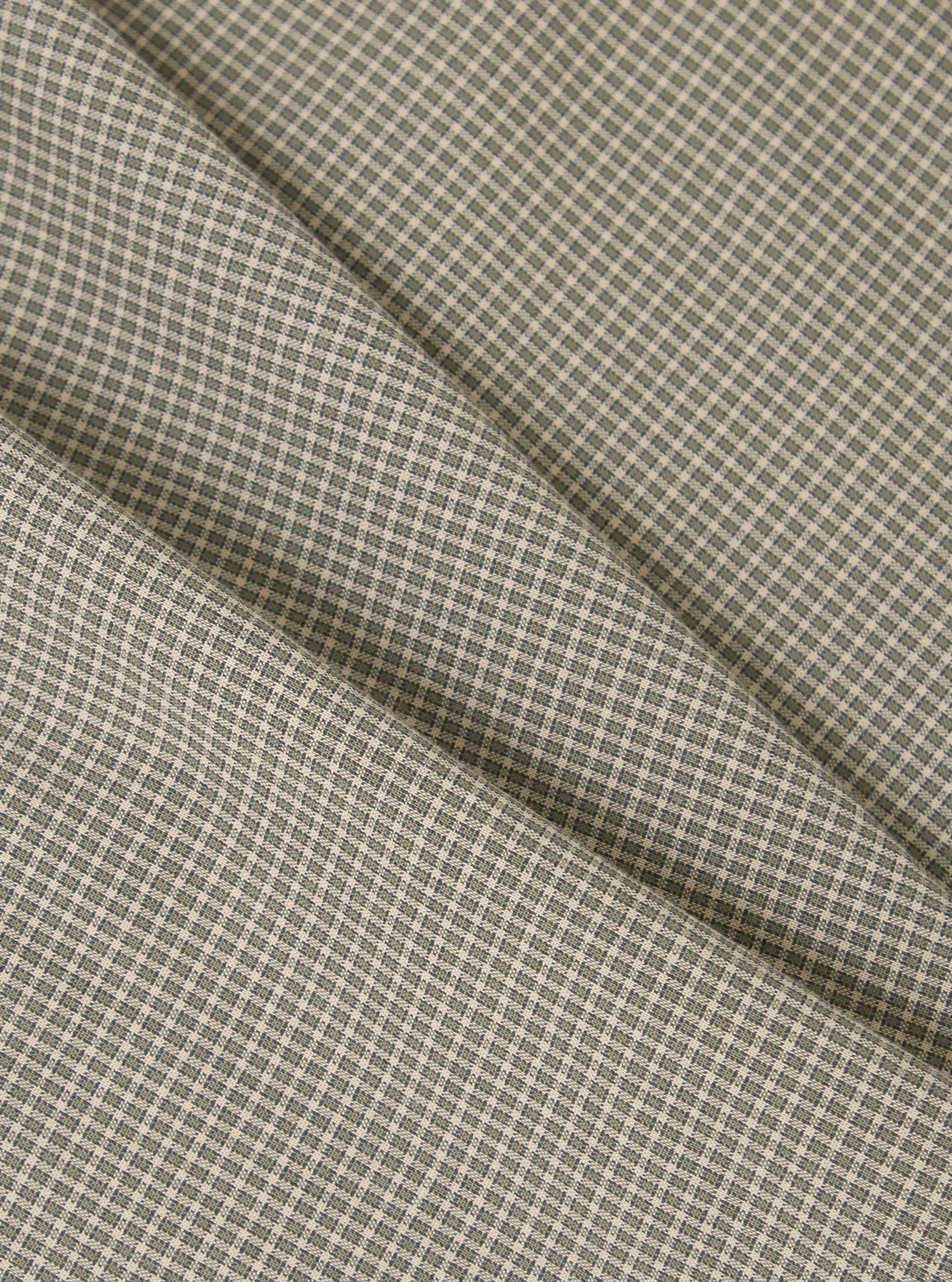 Close-up of the Green Tiny Check Boxer Short fabric. The material is a light beige with a small green check pattern. The fabric is folded on a plain surface.