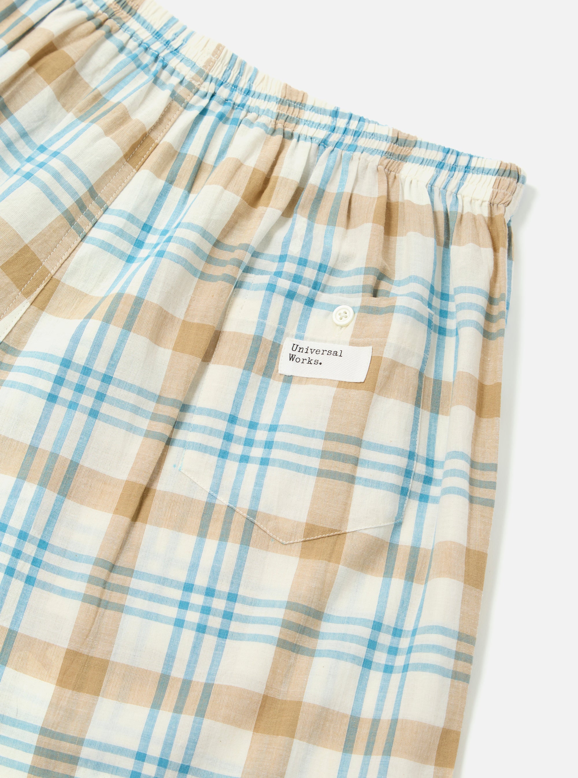 Close-up of the Ecru Madras Check Boxer Short on a white background. The fabric is a light plaid with ecru, tan, and blue lines. Features an elastic waistband and a small pocket.