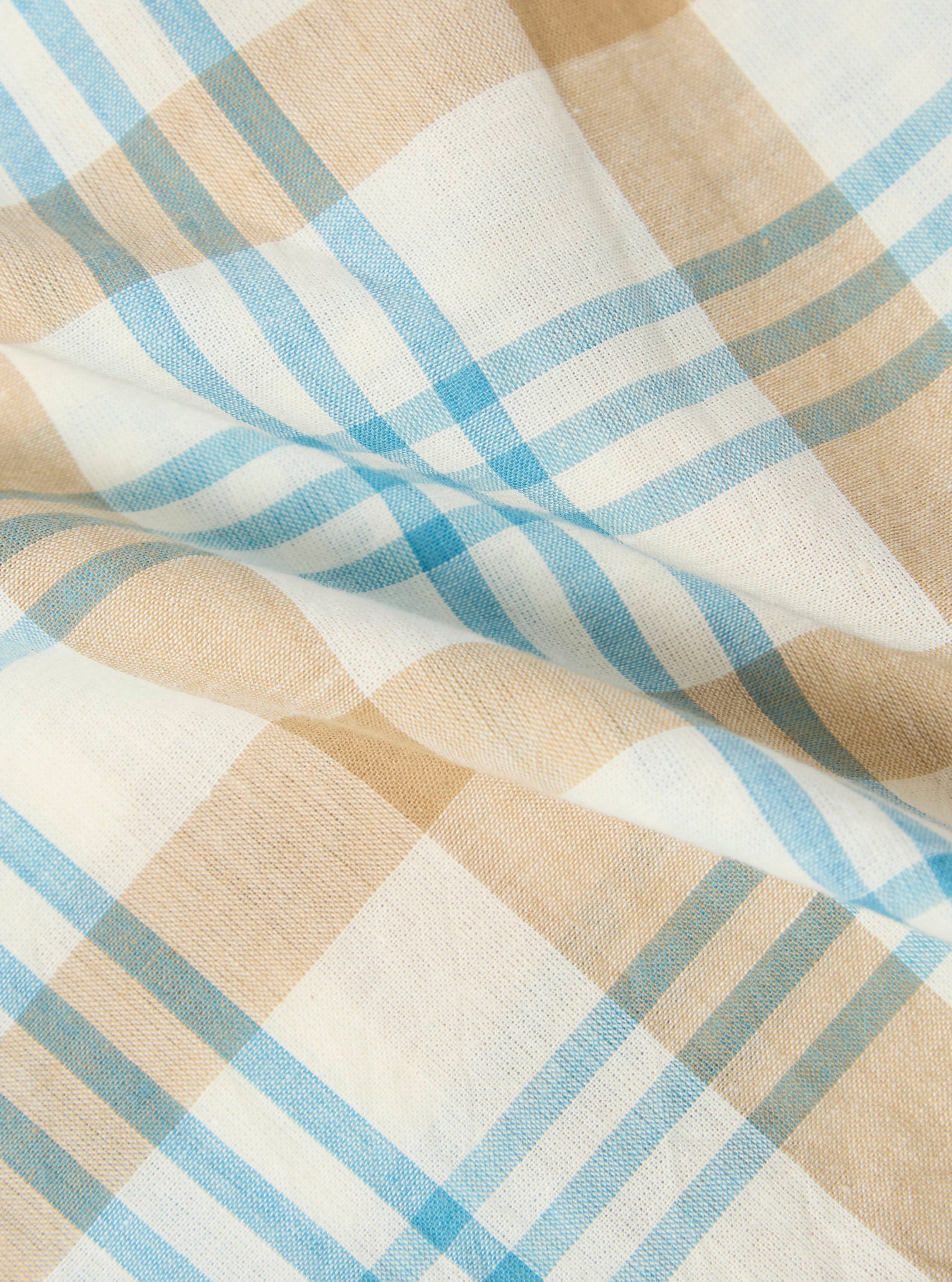 Close-up of the Ecru Madras Check Boxer Short fabric. Features a light blue, tan, and white plaid pattern. The material is slightly wrinkled on a flat surface.