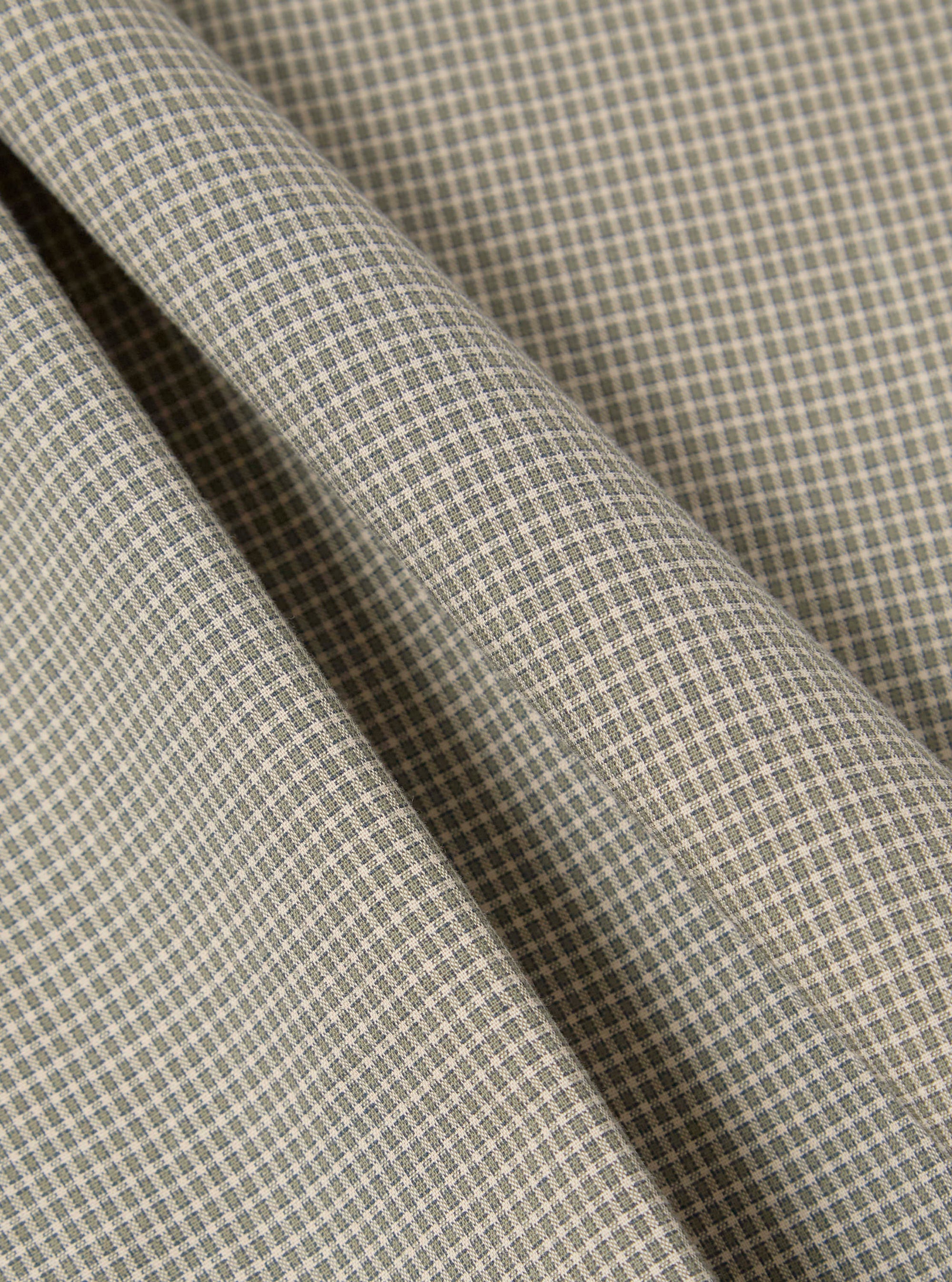 Close-up of the Green Tiny Check Long Pyjama Set fabric. Soft, green and white check pattern. Folded material on a plain surface.