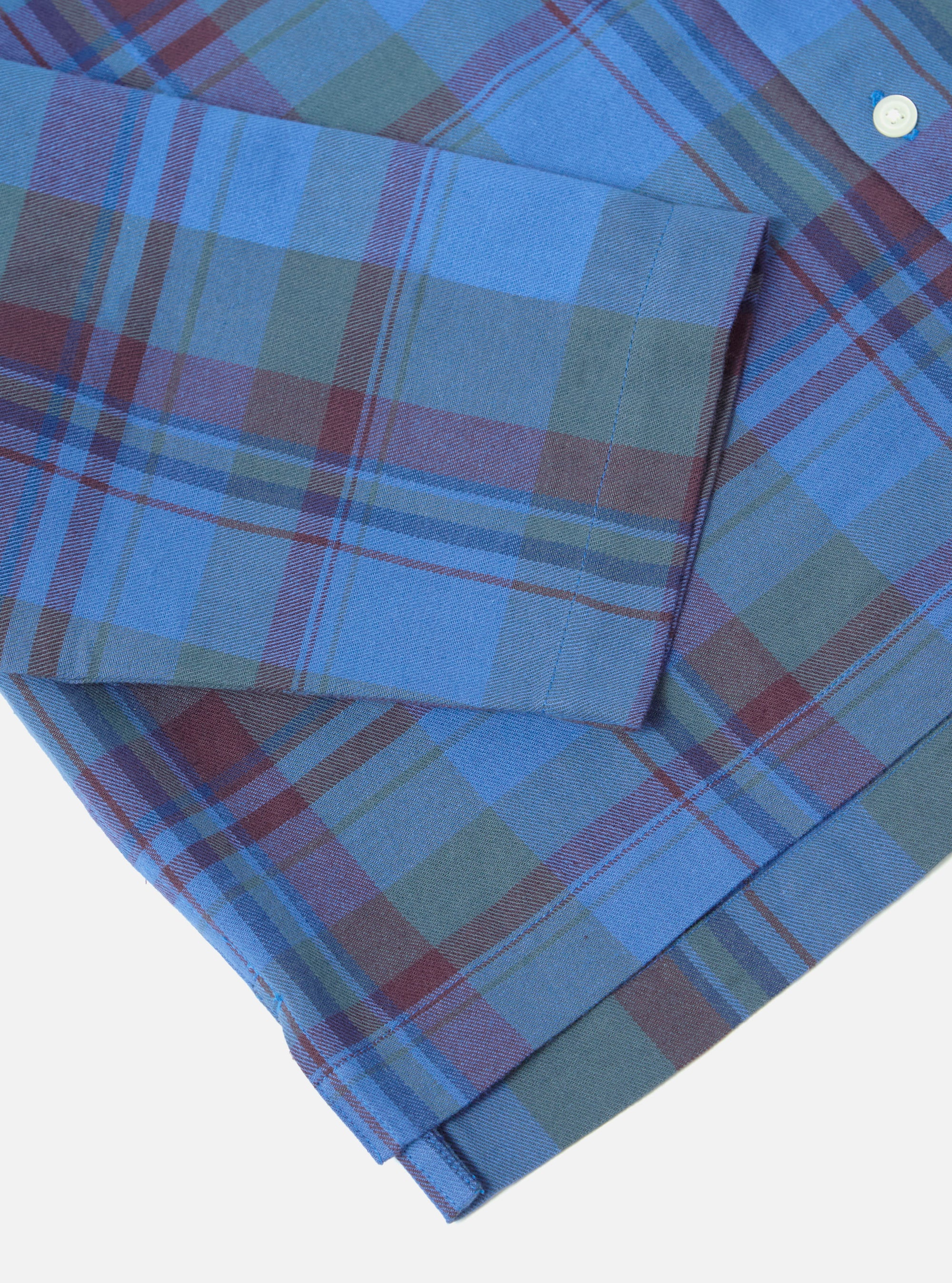 Close-up of the Blue Kip Check Long Pyjama Set on a white surface. The fabric is a blue, green, and burgundy plaid. 