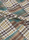 Close-up of the Green Patchwork Madras Pyjama Short fabric. The material is a soft cotton with a green, brown, and white plaid pattern. The fabric is draped on a flat surface.