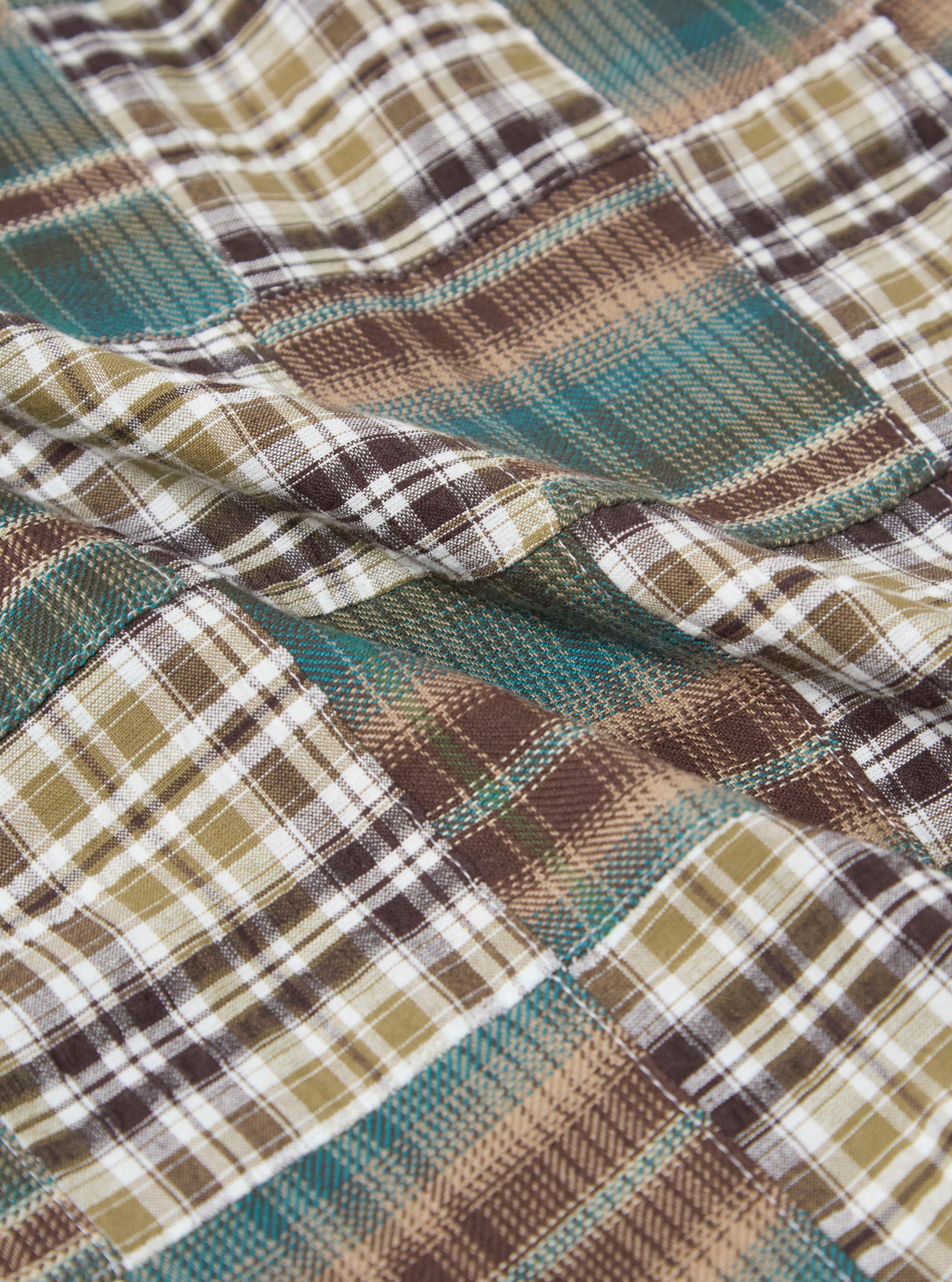 Close-up of the Green Patchwork Madras Pyjama Short fabric. The material is a soft cotton with a green, brown, and white plaid pattern. The fabric is draped on a flat surface.