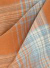 Close-up of folded Orange Check Pyjama Short fabric. Features a soft orange and blue plaid pattern. The material has a subtle texture.