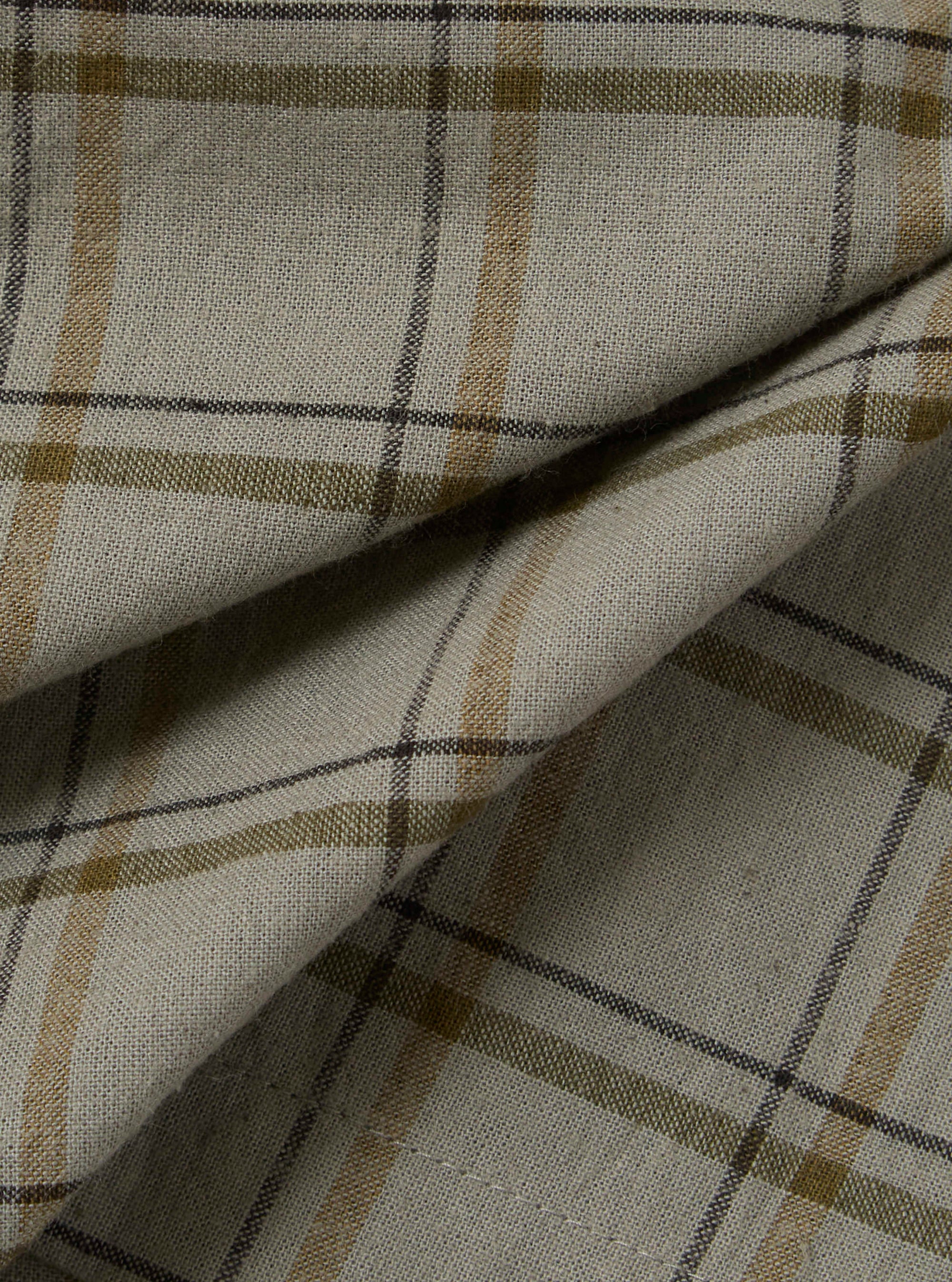 Close-up of the Green PJ Plaid Pyjama Short fabric. The material is a light, neutral tone with green, brown, and black plaid lines. The fabric is folded.