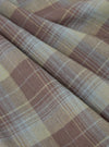 Close-up of the Green/Brown Check Pyjama Pant fabric. The material is folded, showing a detailed plaid pattern in brown, green, and white. The background is a plain surface.