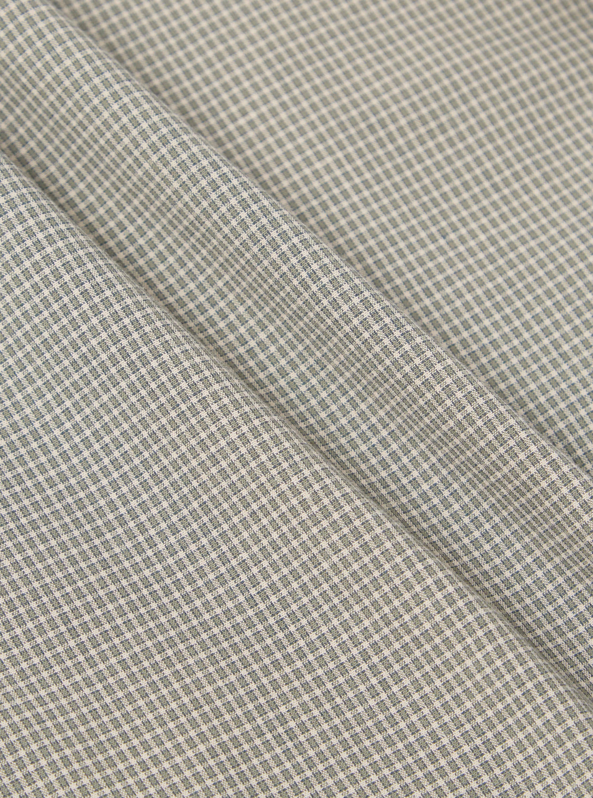 Close-up of the Green Tiny Check Pyjama Pant fabric. The material is a soft green and white tiny check pattern. The fabric is folded on a flat surface.