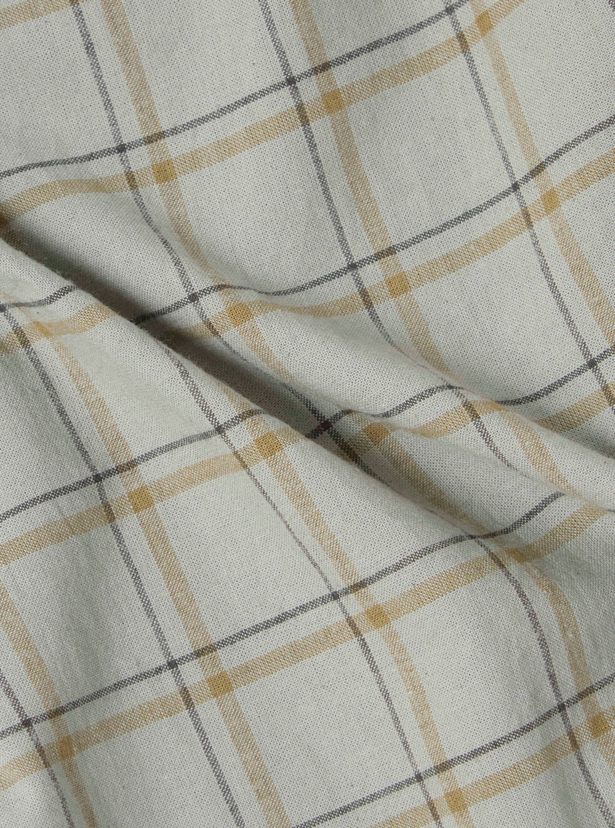 Close-up of the Green PJ Plaid Pyjama Pant fabric. The material is a soft, woven plaid with green, gold, and gray lines on a white background. The fabric is draped on a flat surface.