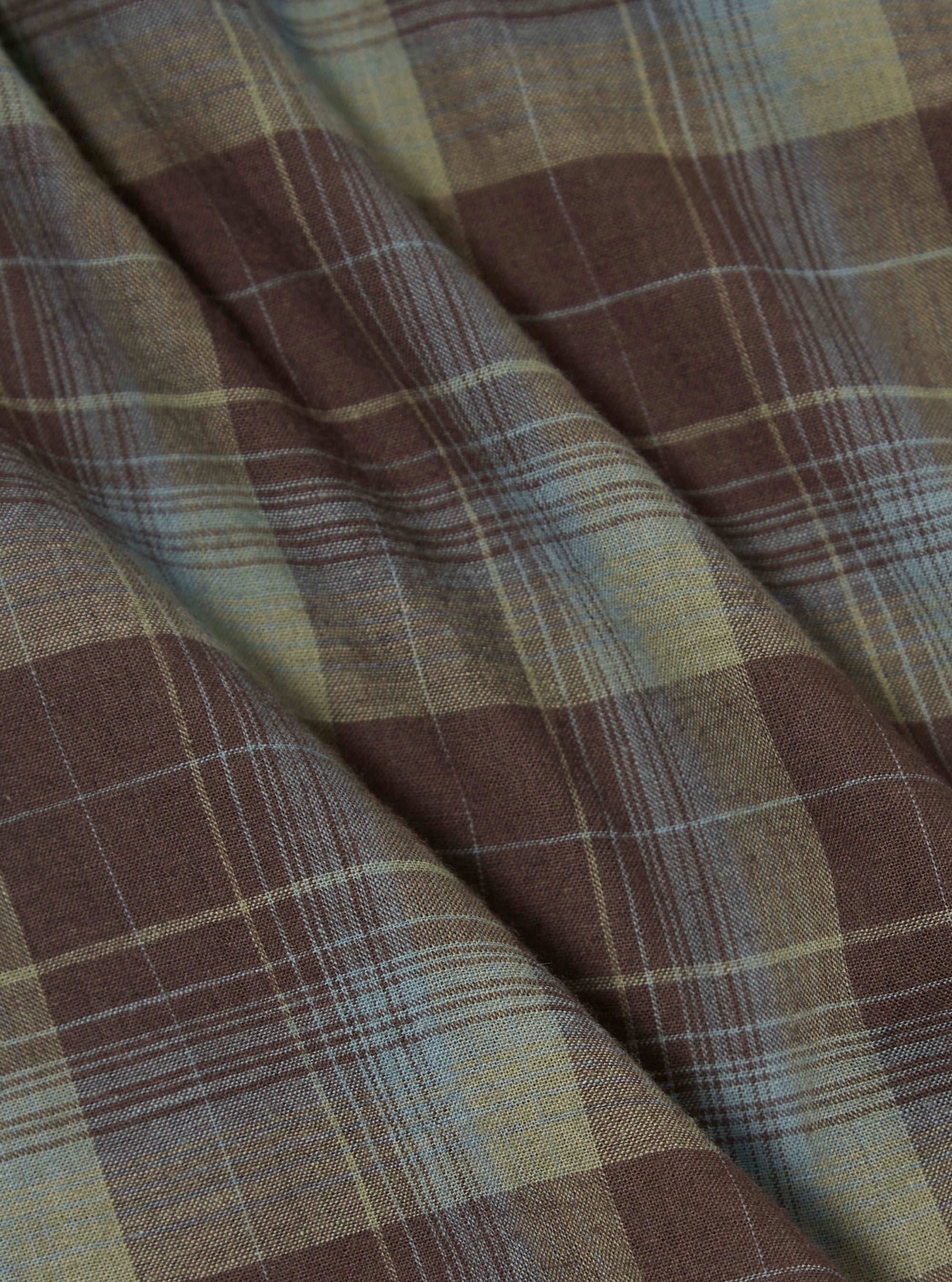 Close-up of the Green Patchwork Madras Boxer Short fabric. Features a brown, green, and blue plaid pattern. The material is folded on a flat surface.