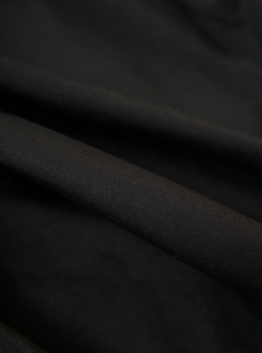 Close-up of the Black Scottish Wax Cotton Boston Parka fabric. The dark, textured material is draped to show its quality and feel. Studio shot.
