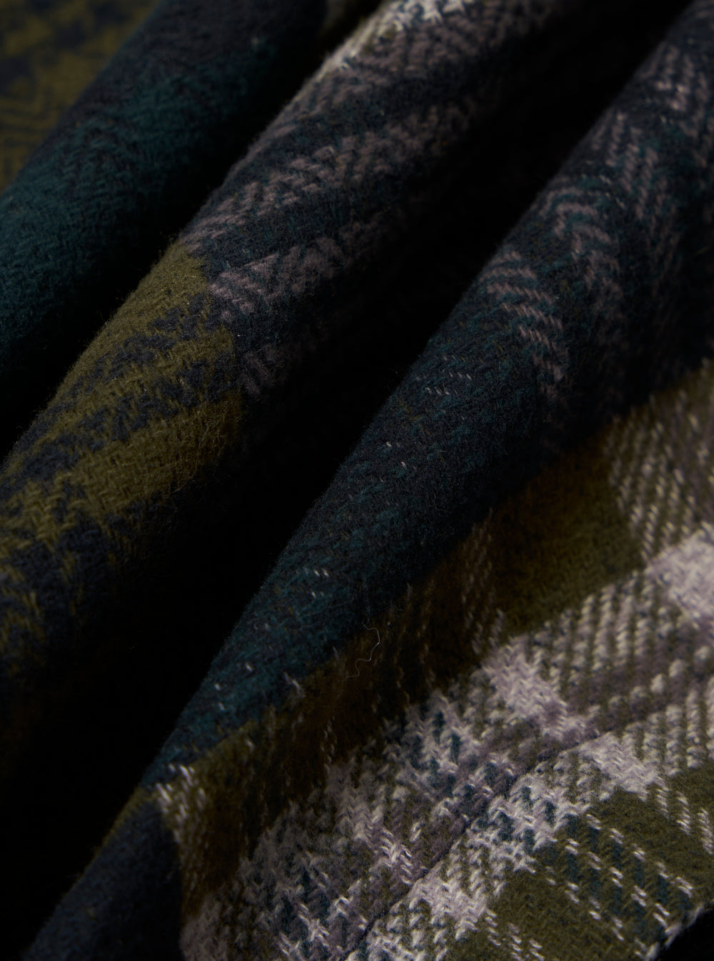Close-up of the Green Japanese Patchwork Dockside Jacket. Features a green, grey, and black patchwork pattern. The fabric is folded and textured.
