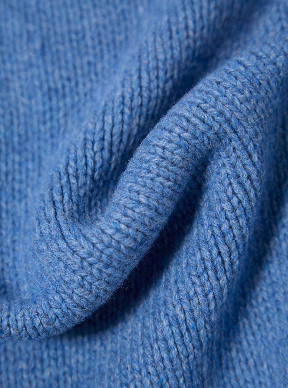 Close-up of the Pale Blue Recycled Shetland Langdale Cardigan, showing the texture and color of the knit. The cardigan is folded on a plain surface.