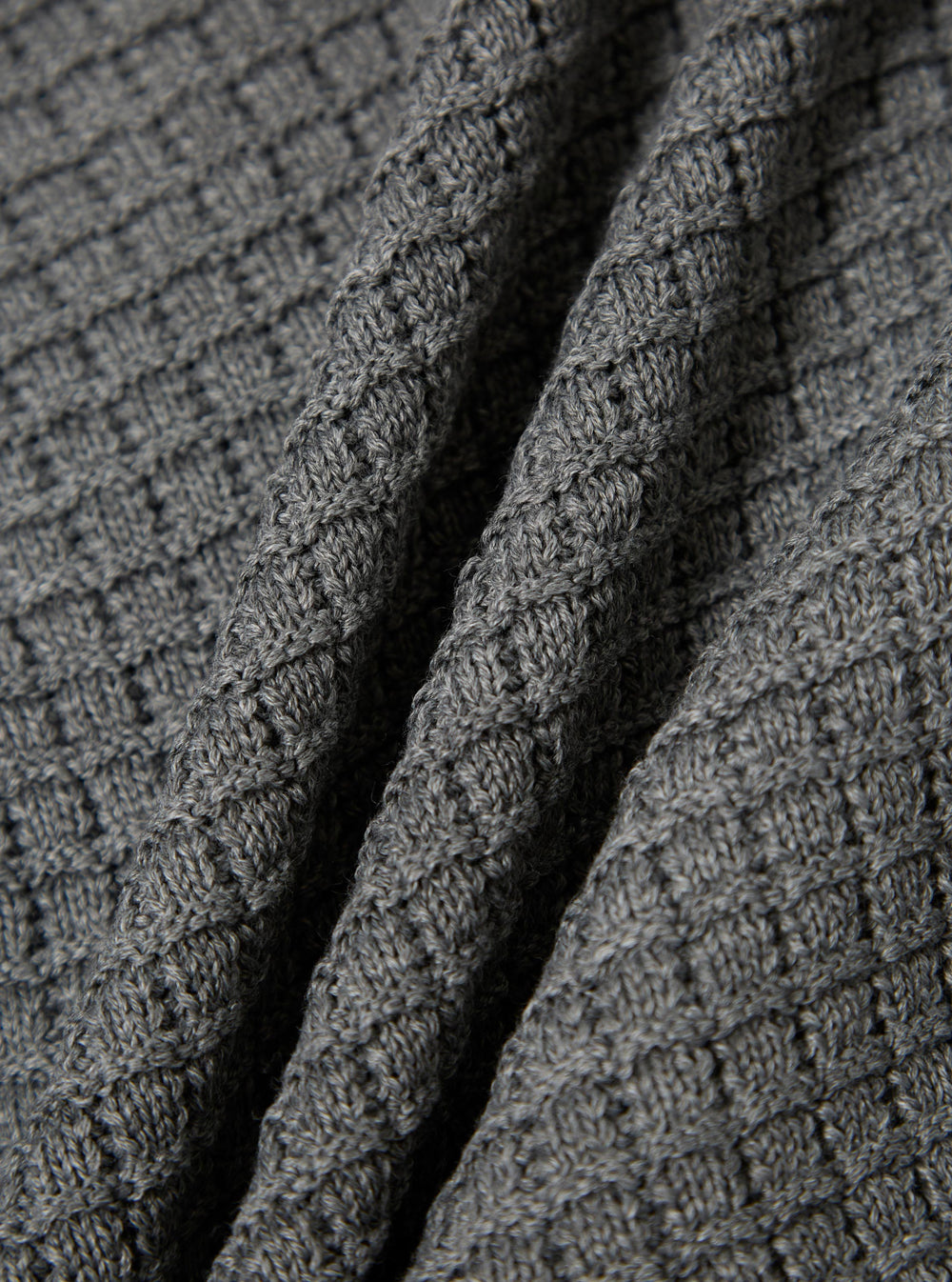 Close-up of the grey textured Merino knit Charlie Cardigan, showing the soft material and detailed knit pattern. The fabric is draped to highlight its texture.