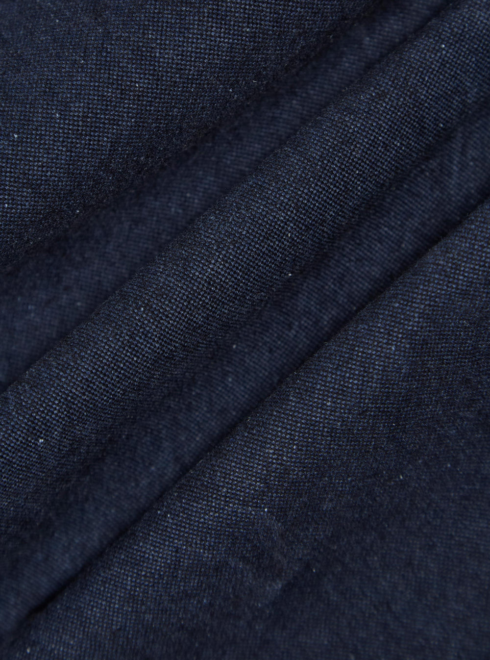 Close-up of the Indigo Offline Denim Duke Pant fabric. The dark blue denim texture is visible, with subtle folds and a plain background.