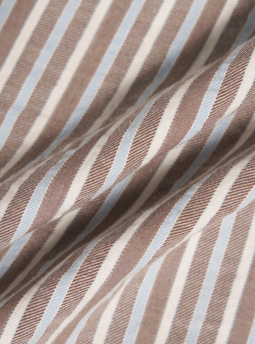 Close-up of the Brown Madison Stripe Station Shirt fabric. Features brown, white, and light blue stripes. The material is folded, showing texture.