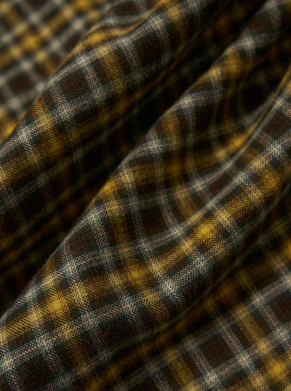 Close-up of the Brown Bang Check Zip Shirt fabric. Features a brown, yellow, and white check pattern. The fabric is draped to show texture.