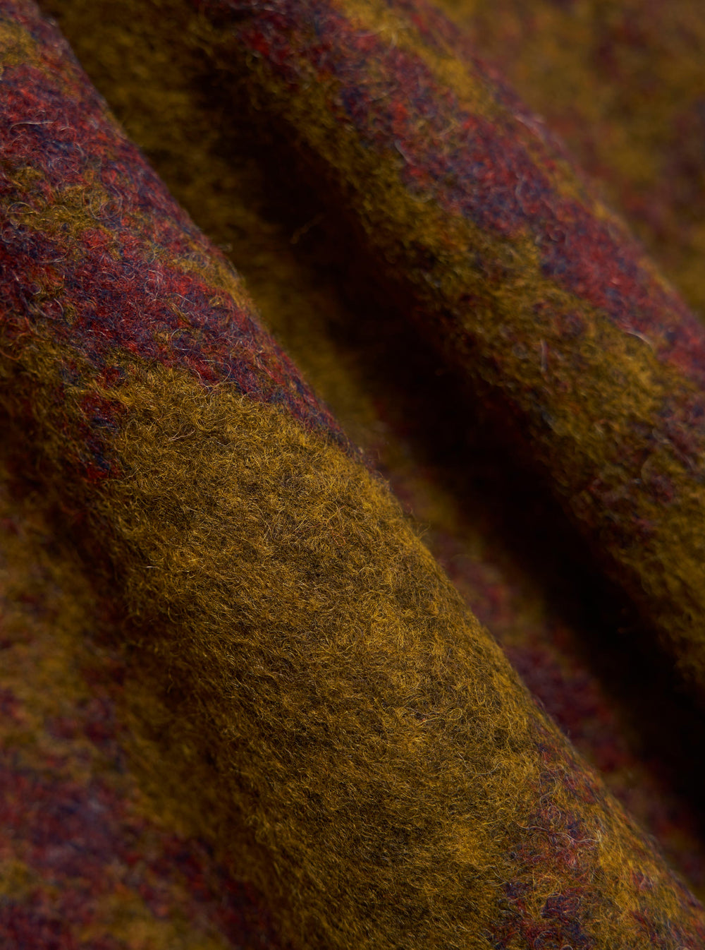 Close-up of the Gold Dam Check Fatigue Shirt fabric. The material is a textured blend of gold, red, and dark blue. The shirt is casually draped on a flat surface.