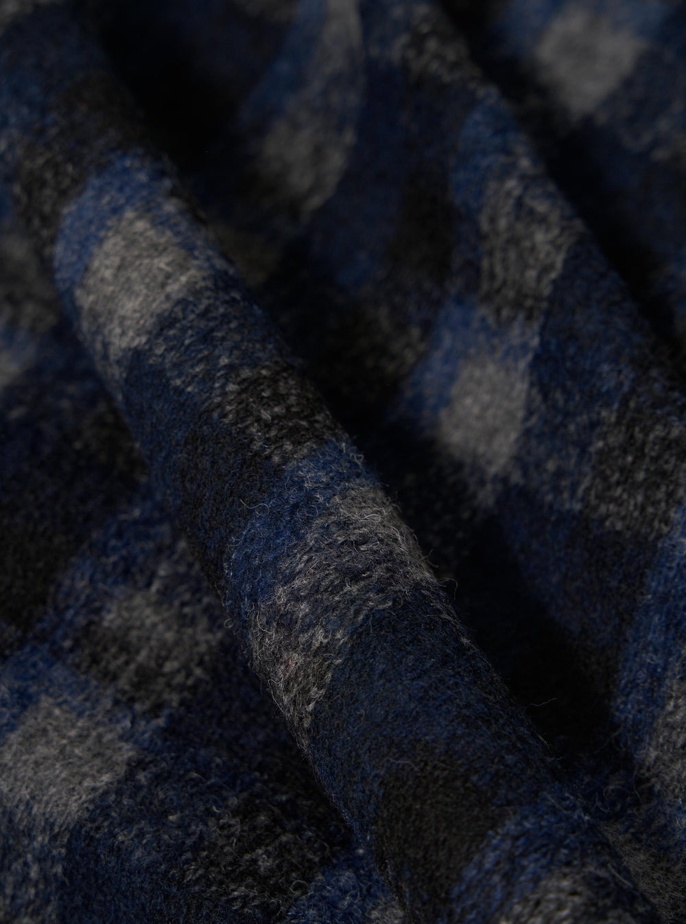Close-up of the Navy/Black Chandler Plaid Fatigue Shirt fabric. The plaid pattern features navy and black hues. The material is textured and folded, showcasing its soft, flannel-like appearance.
