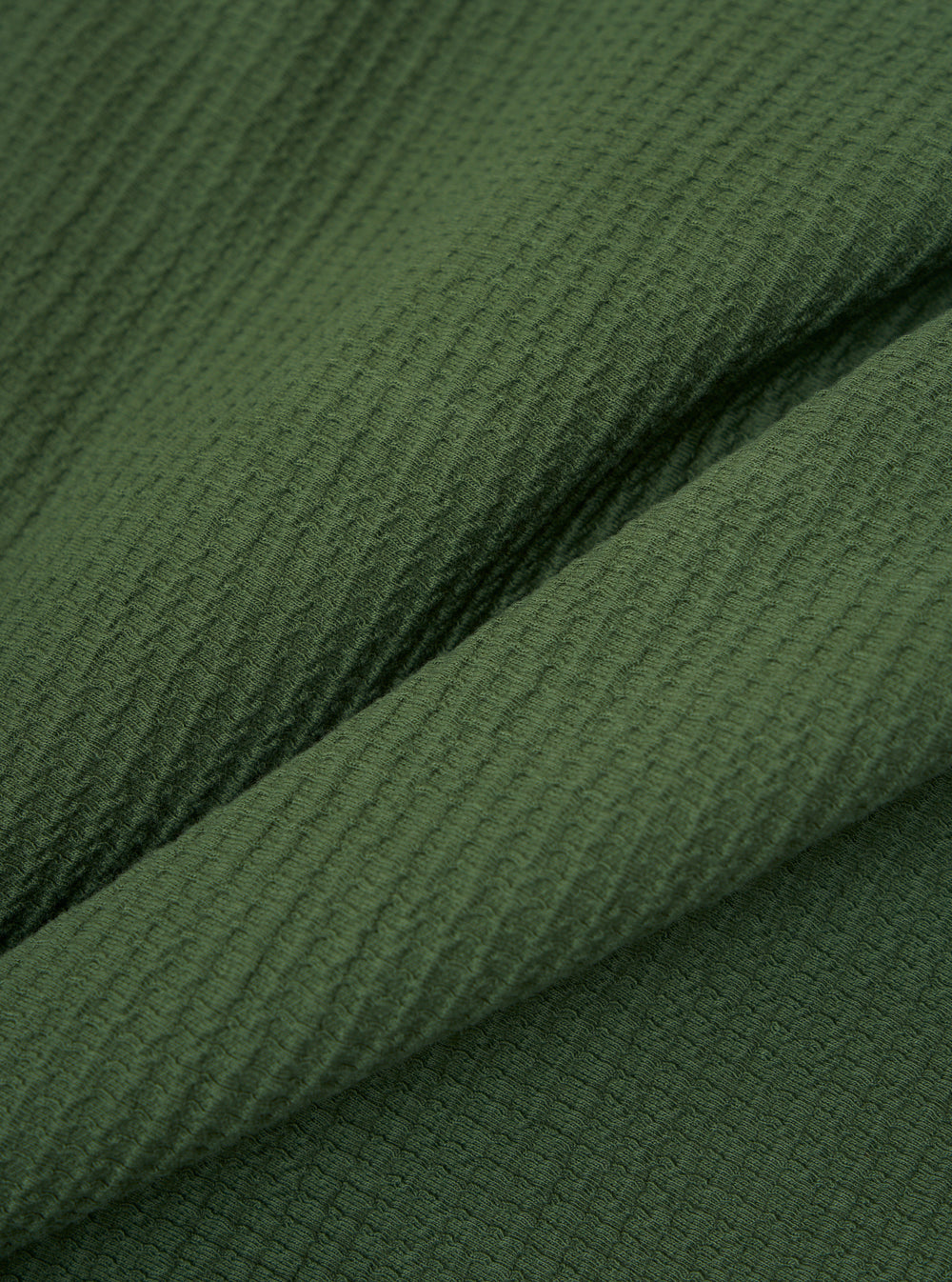 Close-up of the Green Fantasy Interlock K Track Top fabric. The material is textured and green. The image is tightly cropped to highlight the fabric's details.