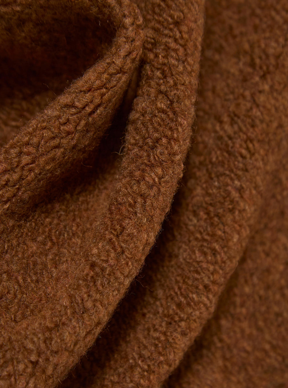 Close-up of the Cumin Alvar Fleece Lancaster Jacket. The soft, brown fleece is draped to show texture. The background is a simple, neutral surface.