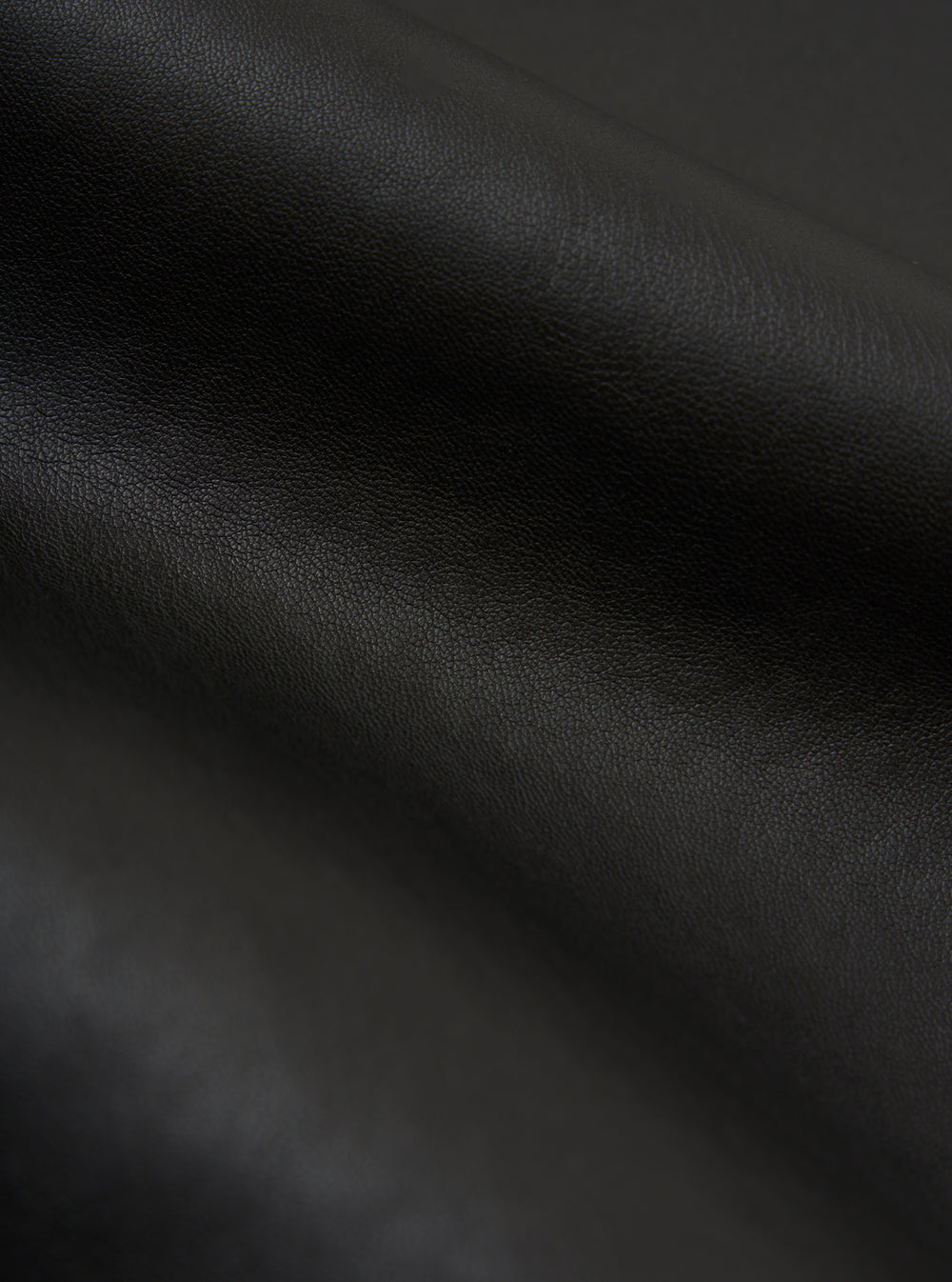 Close-up of the black, textured material of the Black Not Shearling Military Liner Gilet. The fabric is draped on a neutral surface, highlighting its supple texture.