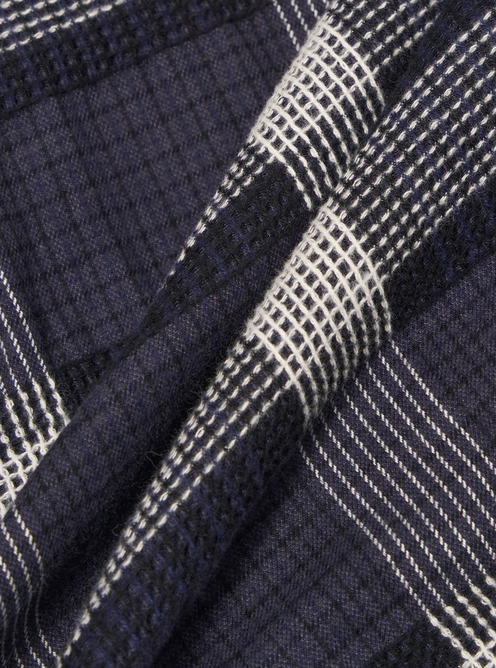 Close-up of the Charcoal Polka Check Easy Overshirt fabric. The material is a dark charcoal with a white polka check pattern. The fabric is folded and textured.
