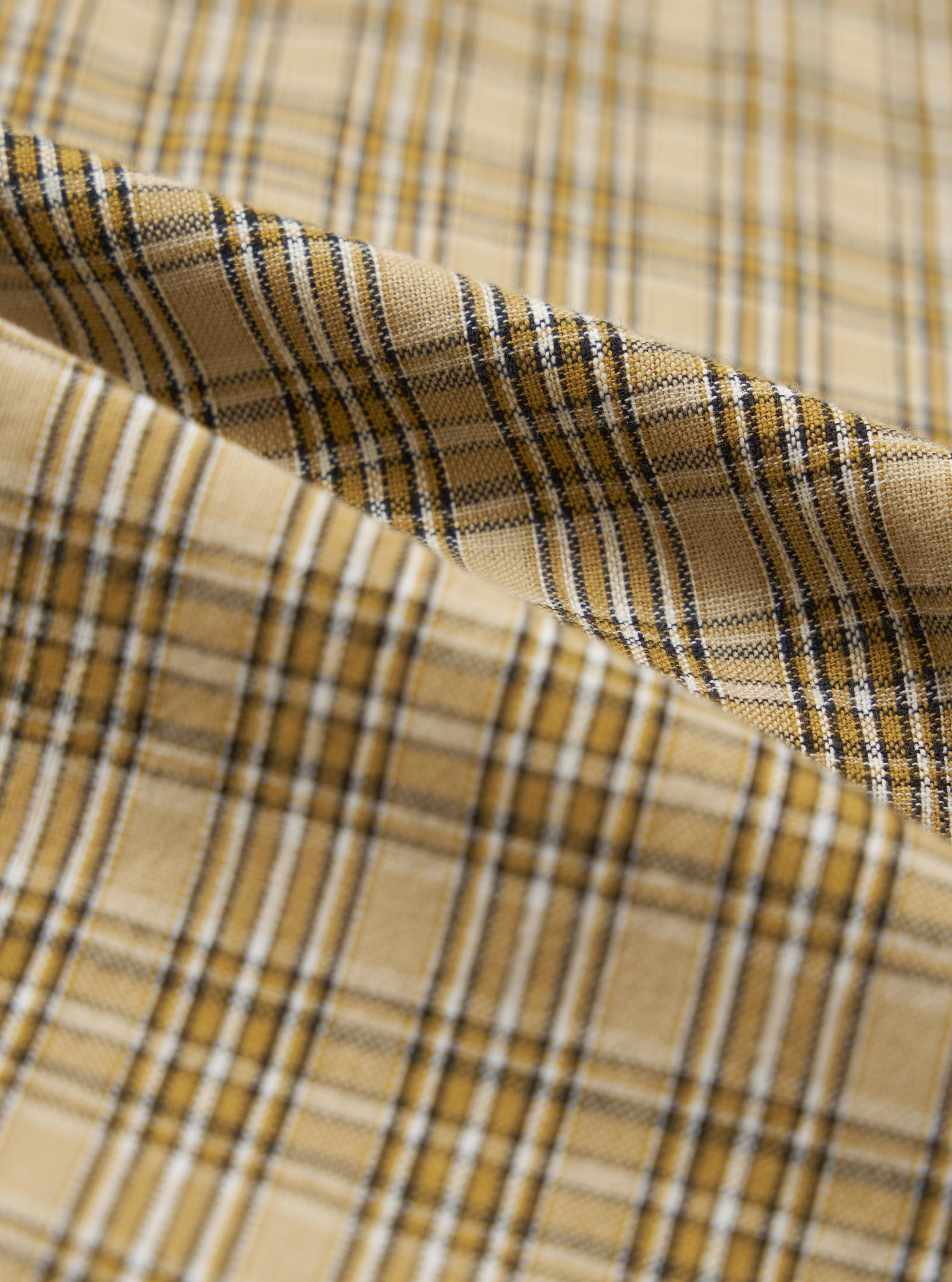 Close-up of the Sand Picnic Plaid Pyjama Pant fabric. The material is a soft, woven plaid in shades of sand, gold, white, and black. The fabric is draped to show texture.