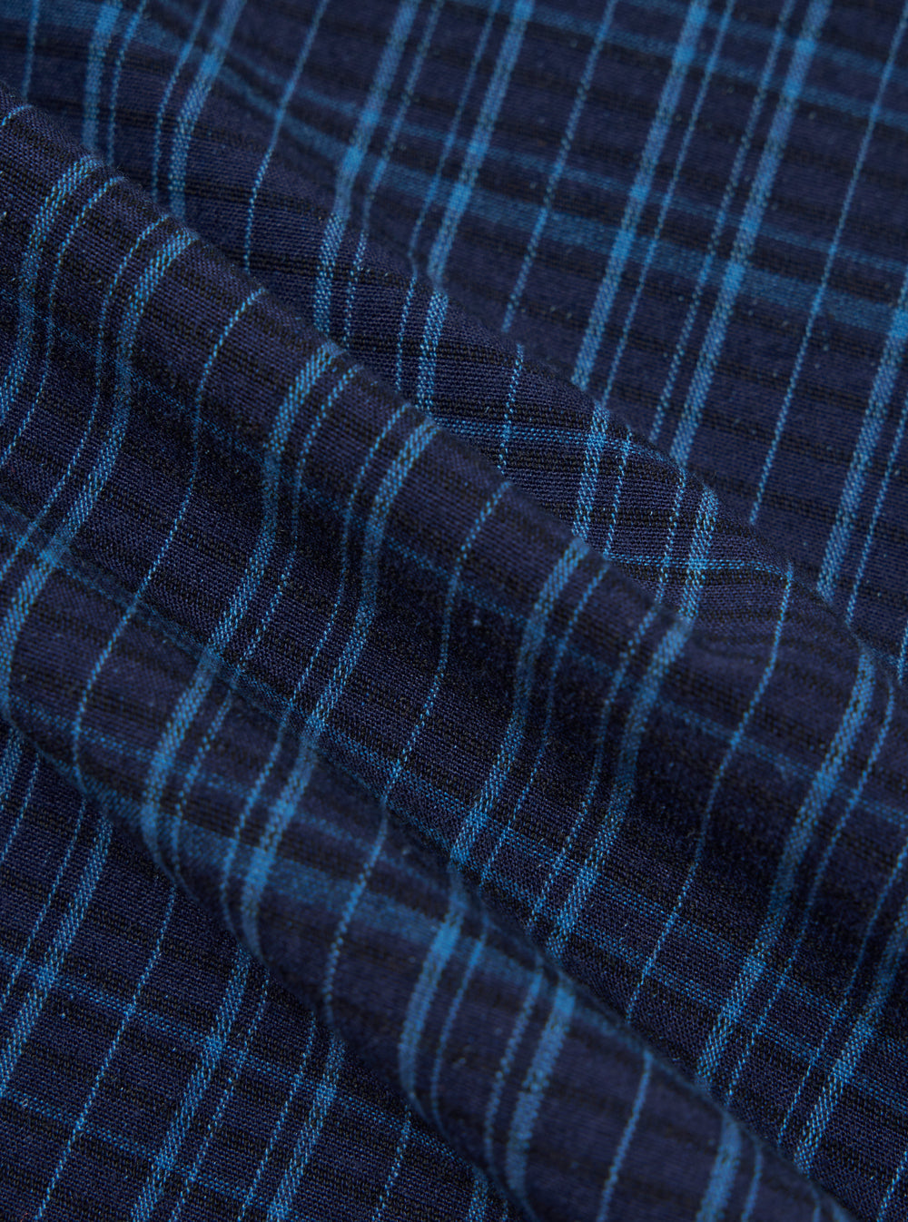 Close-up of the Indigo Plaid Long Pyjama Set fabric. The material is a soft, woven plaid in shades of indigo and light blue. The fabric is draped to show texture.