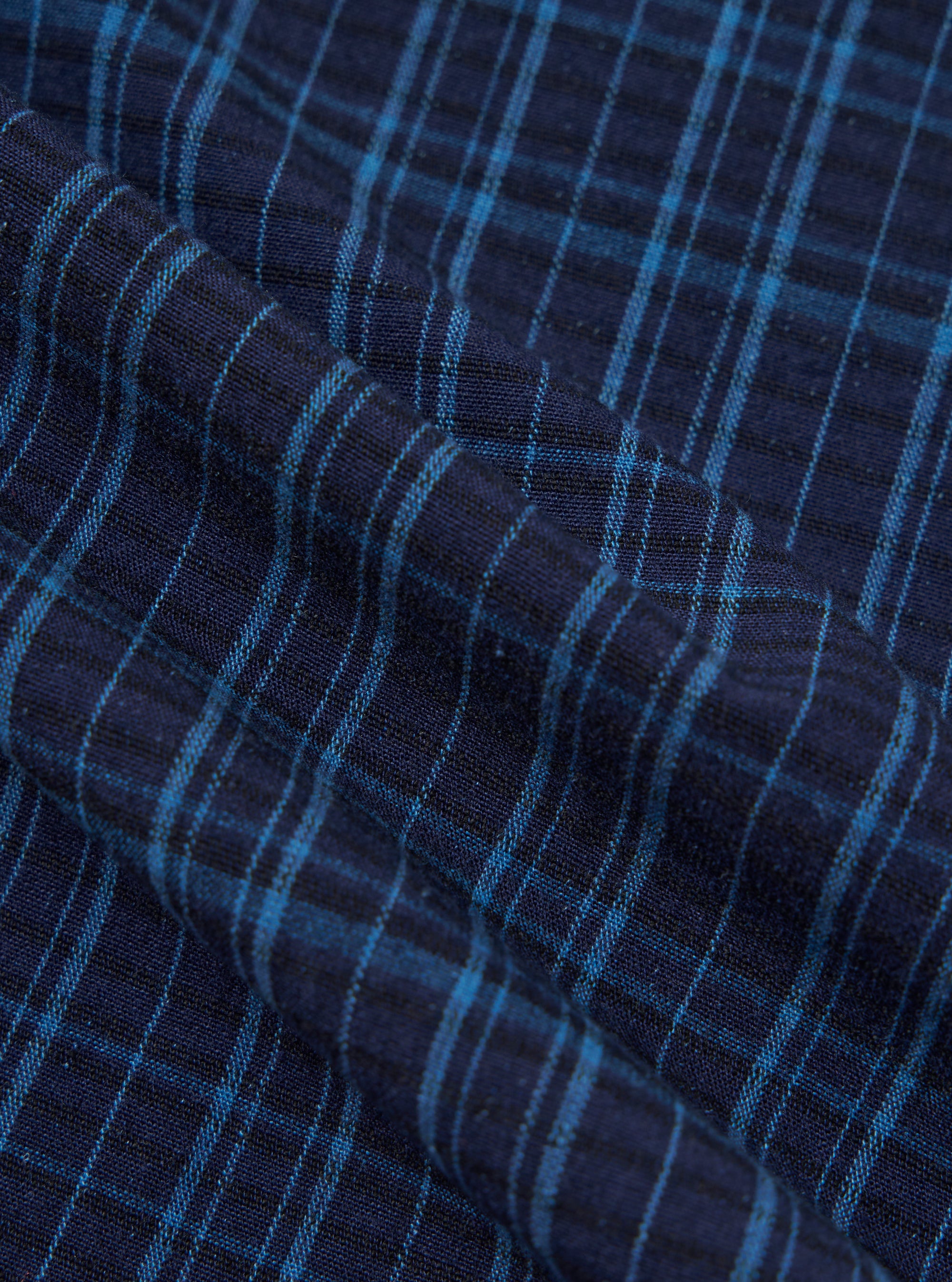 Close-up of the Indigo Plaid Long Pyjama Set fabric. The material is a soft, woven plaid in shades of indigo and light blue. The fabric is draped to show texture.