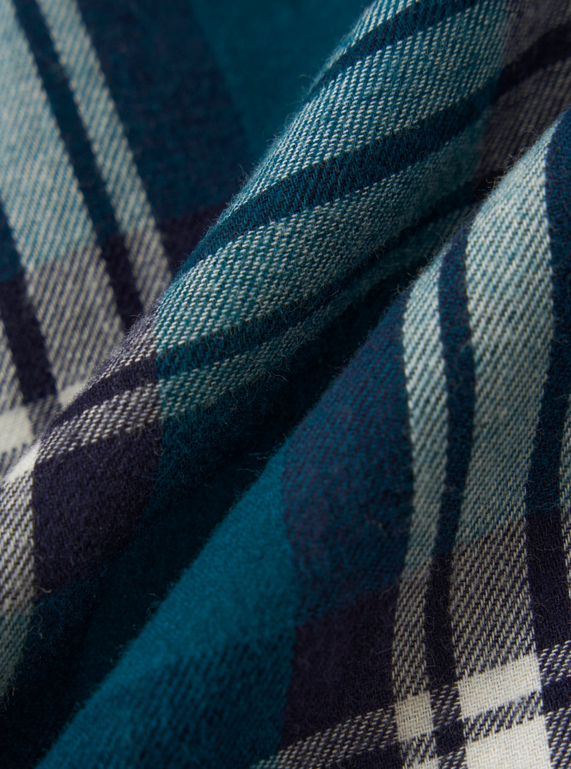 Close-up of the Forest Brushed Plaid Pyjama Short fabric. The brushed cotton is teal, navy, and white in a classic plaid pattern. The fabric is softly folded.
