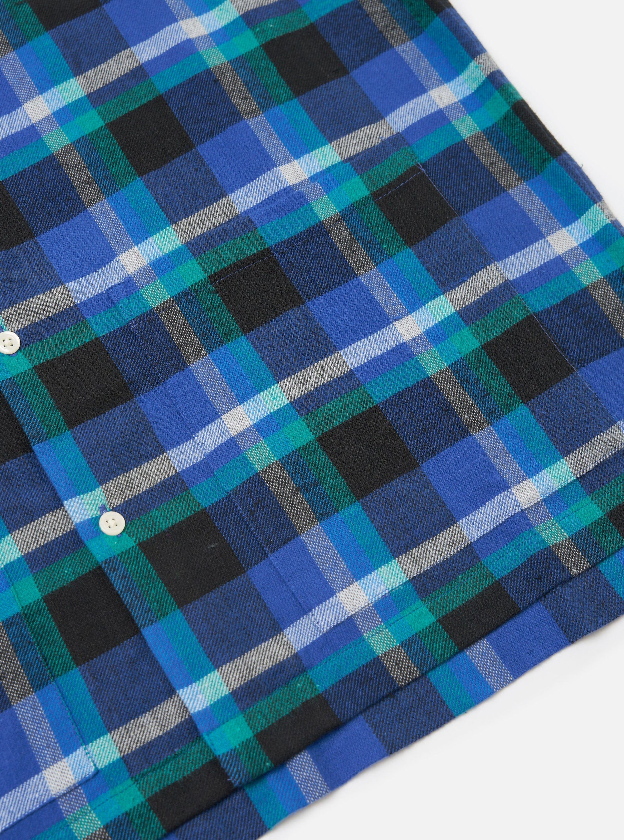 Close-up of the Blue Night Check Short Pyjama Set. Features a blue, green, black and white plaid pattern. The fabric is neatly laid out on a white surface.