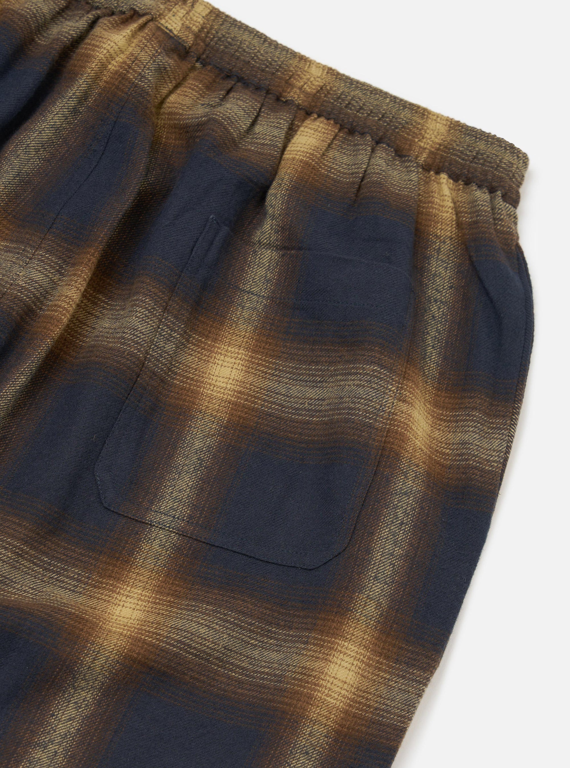 Close-up of the Navy Canyon Check Pyjama Pant on a white surface. The fabric is a soft, brushed cotton in a navy and tan check pattern. Features an elastic waistband and a back pocket.