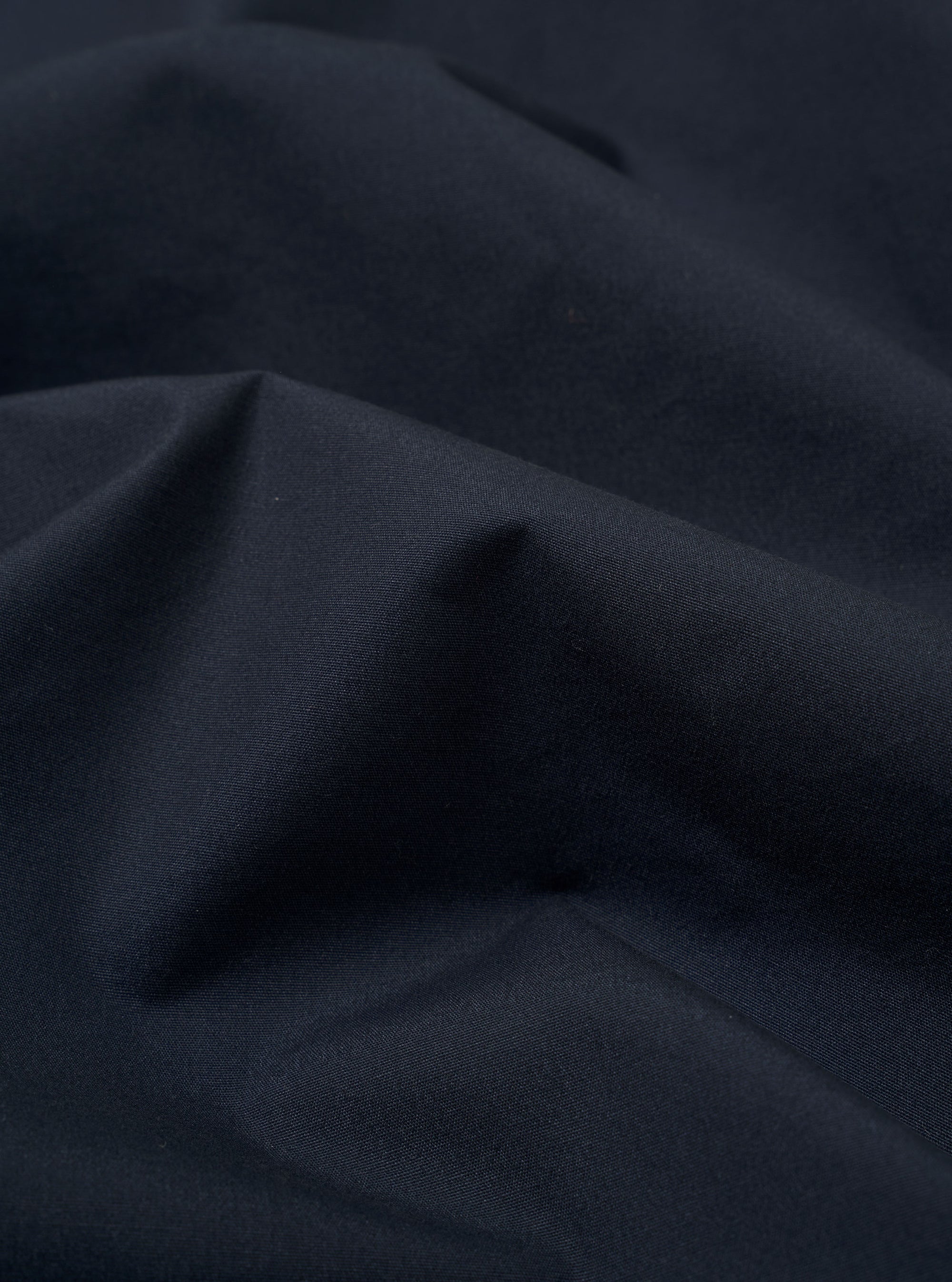 The Navy Recycled Polytech Bakers Jacket is displayed as a flat lay against a plain white background. The jacket features a classic collar, a five-button front closure, and multiple patch pockets, including one on the chest and two larger ones at the waist. The hem is slightly curved at the front.