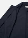 The Navy Recycled Polytech Bakers Jacket is shown in a close-up detail shot as a flat lay against a plain white background. The image focuses on the lower front corner of the jacket, showcasing a large rectangular patch pocket and the clean stitching along the hem and side. The deep navy blue fabric has a smooth, matte finish.