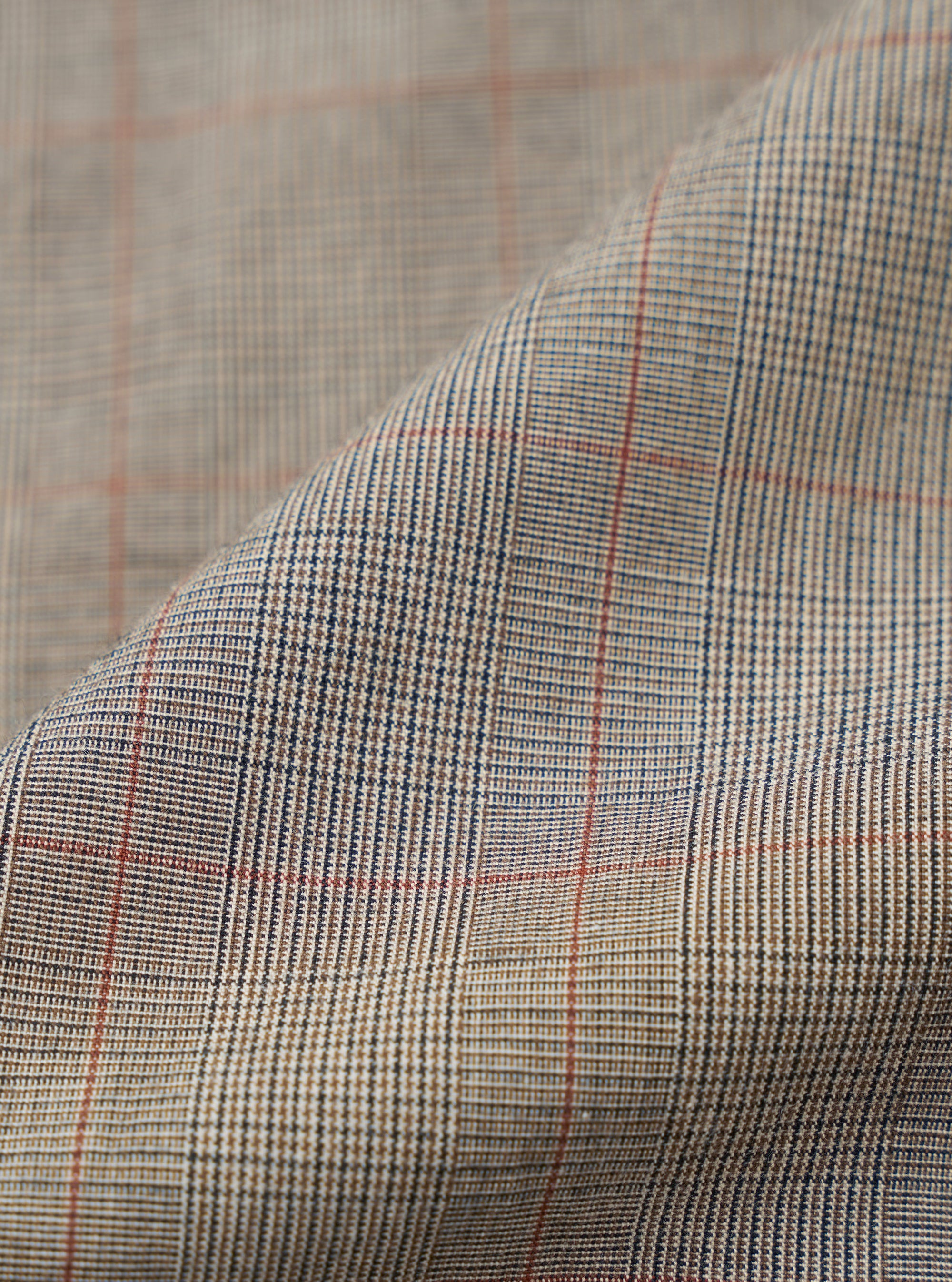 A close-up fabric swatch of the Grey Brown Wales Glen Check Barra Jacket highlights the classic Prince of Wales check pattern. The intricate weave features a mix of grey, brown, and black threads, creating a textured and sophisticated geometric design.