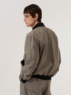 The Grey Brown Wales Glen Check NS Bomber Jacket is worn by a model against a plain white background. The image, captured from the rear, highlights the jacket's relaxed fit and the intricate grey and brown glen check pattern. The garment features a ribbed collar, cuffs, and hem, with a clean, straight-cut back panel. No mannequin is present in the image.