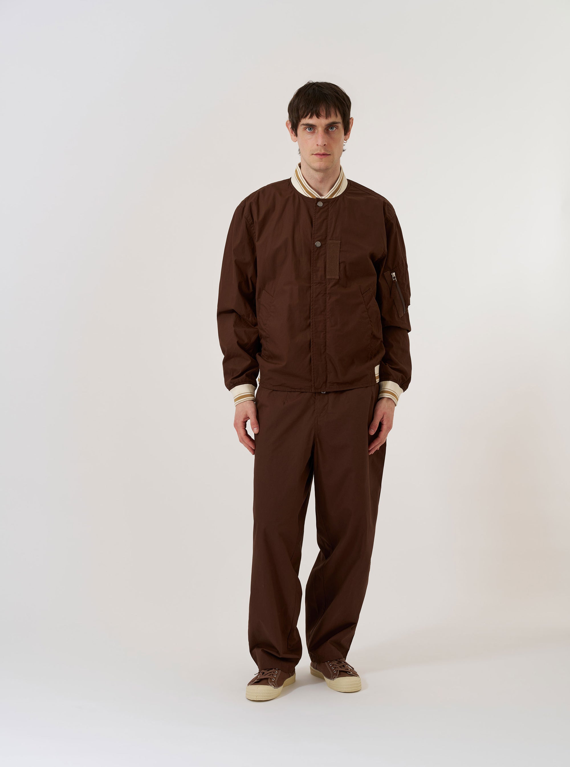 The Brown Peached Poplin NS Bomber Jacket is shown as a flat lay against a plain white background. The jacket features a central zip-front closure, two slanted welt pockets at the waist, and a ribbed collar, cuffs, and hem. The peached cotton poplin fabric has a smooth, matte brown finish.