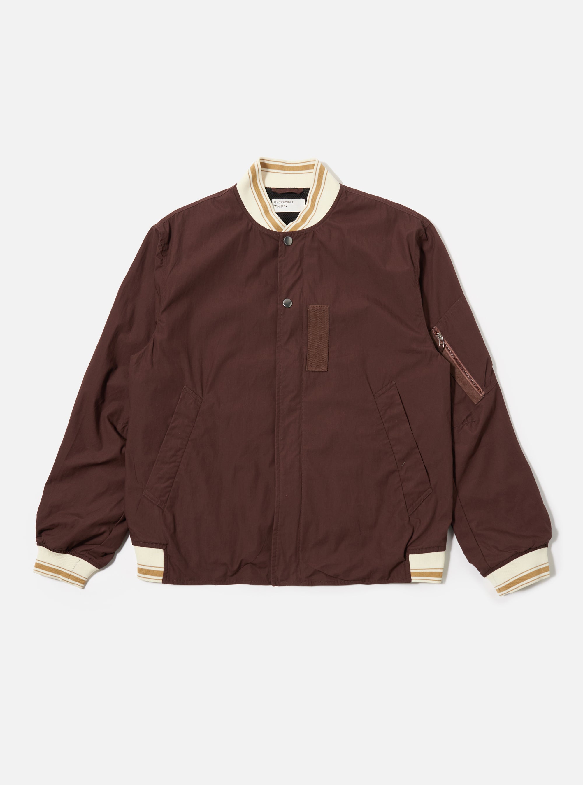 The Brown Peached Poplin NS Bomber Jacket is shown as a flat lay against a plain white background. The jacket features a central zip-front closure, two slanted welt pockets at the waist, and tonal ribbed detailing at the collar, cuffs, and hem. The cotton peached poplin fabric has a smooth, matte finish in a solid brown color.