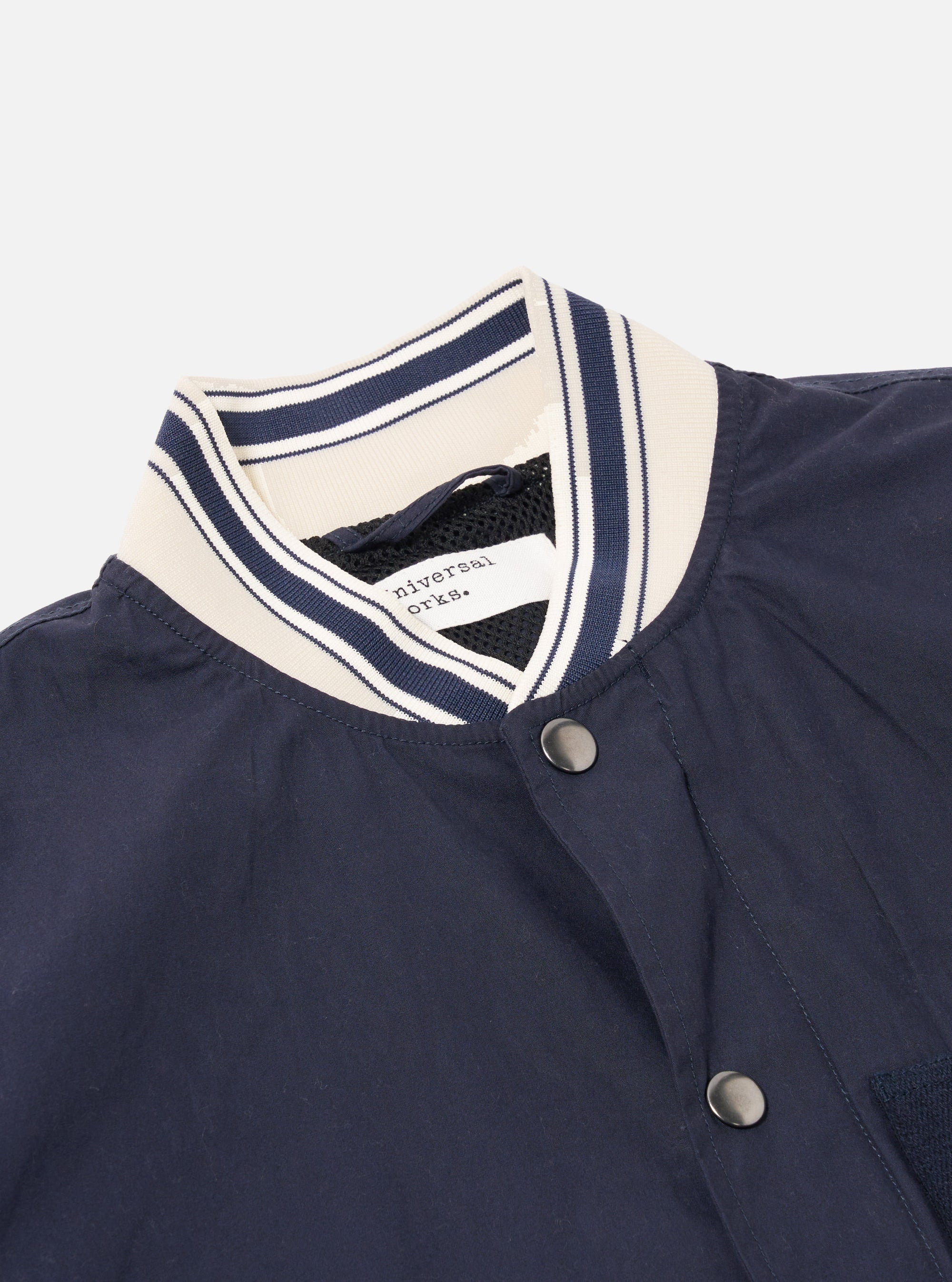 The Navy Peached Poplin NS Bomber Jacket is shown from the back as a flat lay against a plain white background. The image highlights the jacket's smooth navy cotton poplin fabric, a central vertical seam, and the contrast stripe ribbing on the collar, cuffs, and hem.
