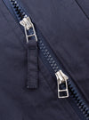 The Navy Peached Poplin NS Bomber Jacket is shown as a flat lay against a plain white background. The jacket features a central zip front with a buttoned placket, a ribbed collar, and a utility zip pocket on the left sleeve. Two large hand warmer pockets are visible on the front, and the fabric has a smooth, matte finish.