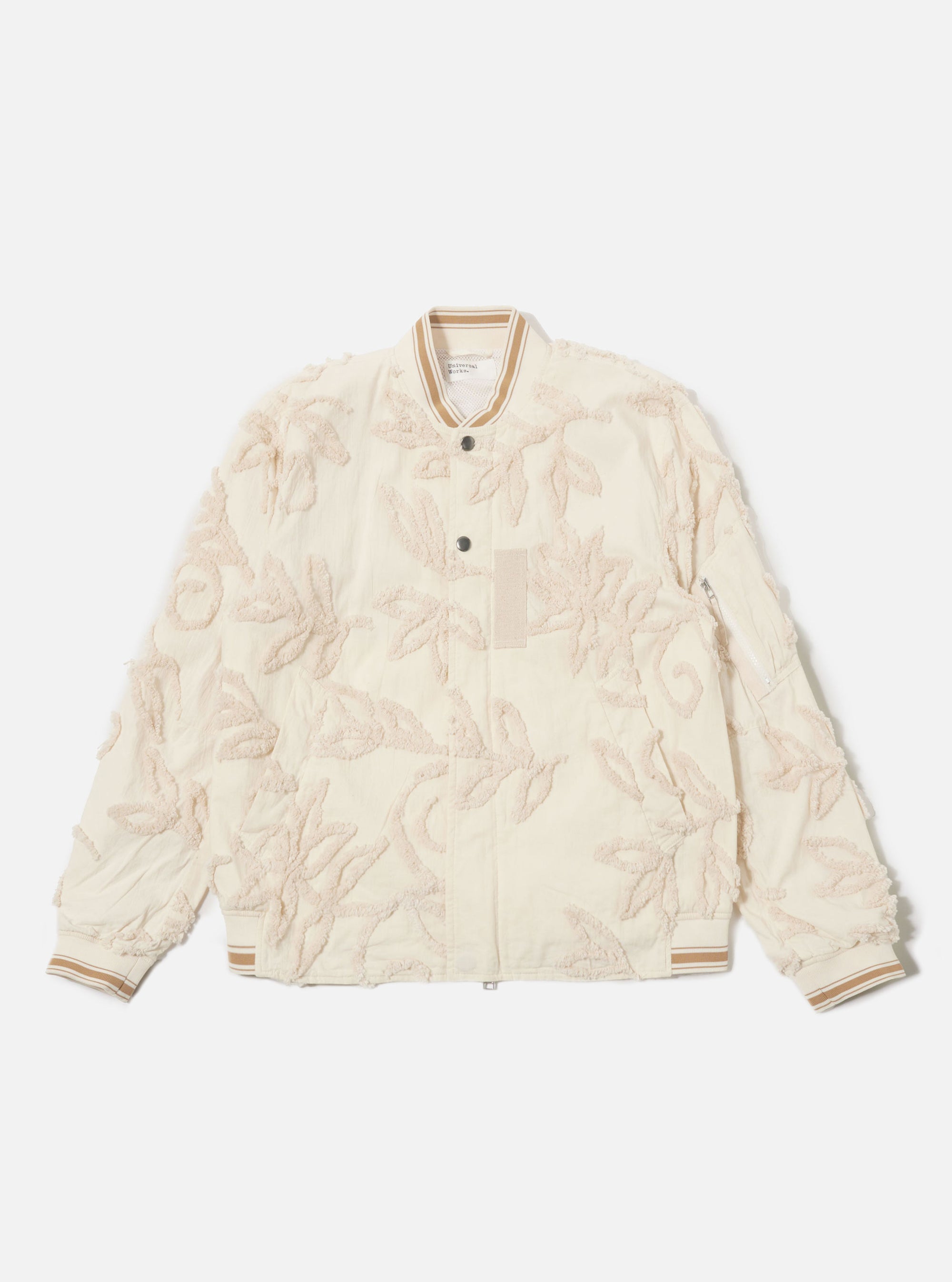 The Ecru 3D Flower NS Bomber Jacket is shown as a flat lay against a plain white background. The jacket features an intricate all-over 3D floral texture in an ecru shade, a central two-way zip closure with a buttoned placket, and contrast stripe ribbing on the collar, cuffs, and hem. A prominent zipped utility stash pocket is visible on the left sleeve.