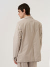 A model wears the Brown Kennedy Stripe Boston Blazer over a neutral-colored shirt, shown from a rear three-quarter angle against a plain, light grey background. The blazer features a vertical striped pattern in shades of brown and white, a structured back with a single central vent, and a relaxed tailored fit. The texture of the cotton fabric is visible under studio lighting.