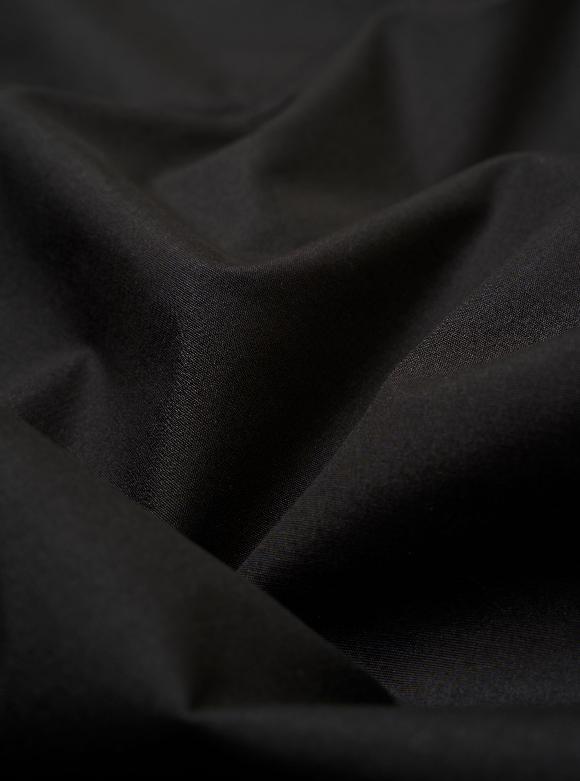 The Black Recycled Polytech Capitol Jacket is shown from a rear three-quarter angle as a flat lay against a plain white background. The image highlights the jacket's unstructured design, featuring a single back vent and a smooth black fabric with a subtle technical sheen.